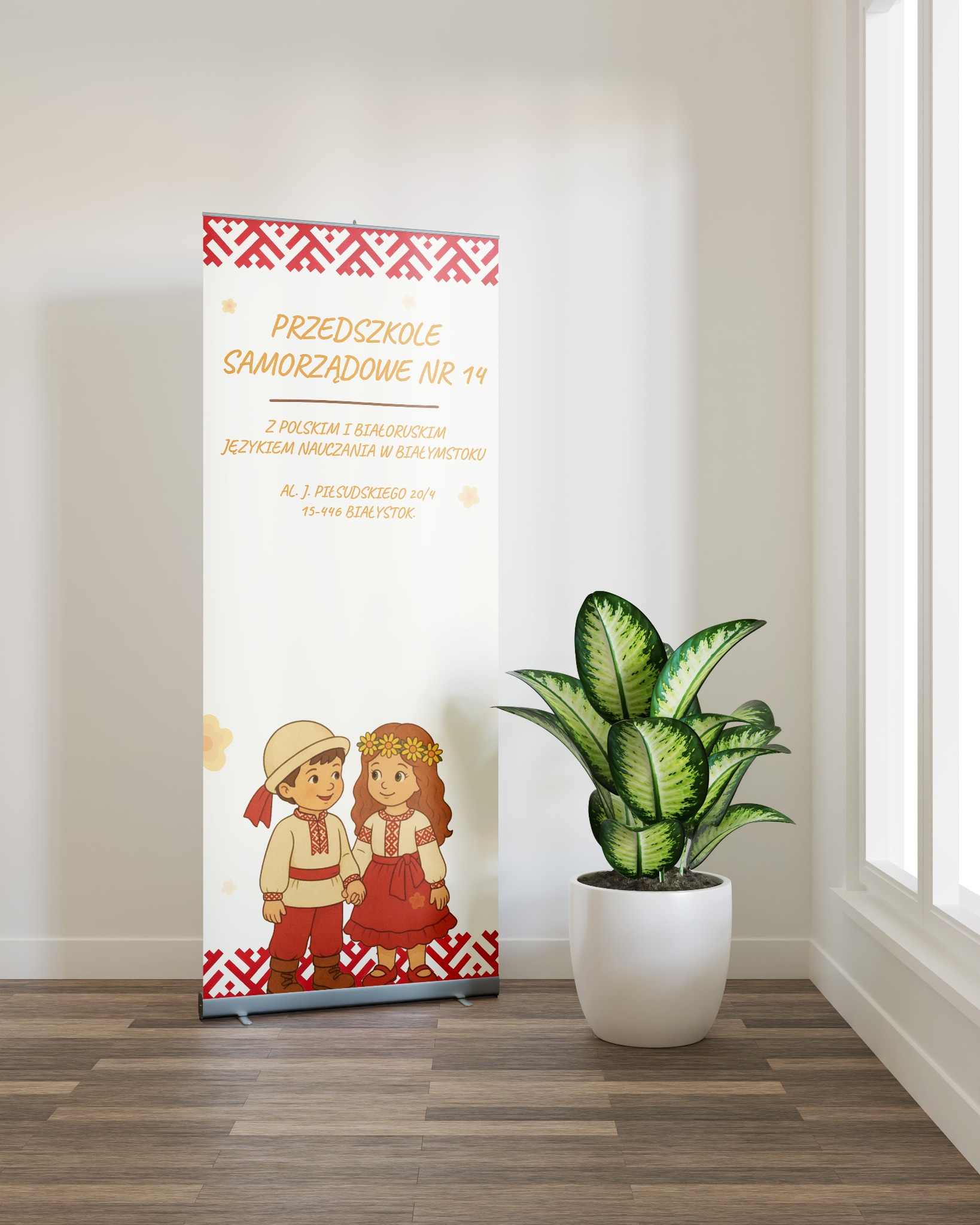 Roll-up z grafiką przedszkola samorządowego nr 14, z motywami ludowymi i ilustracjami dzieci w strojach regionalnych, stojący obok rośliny doniczkowej przy oknie.