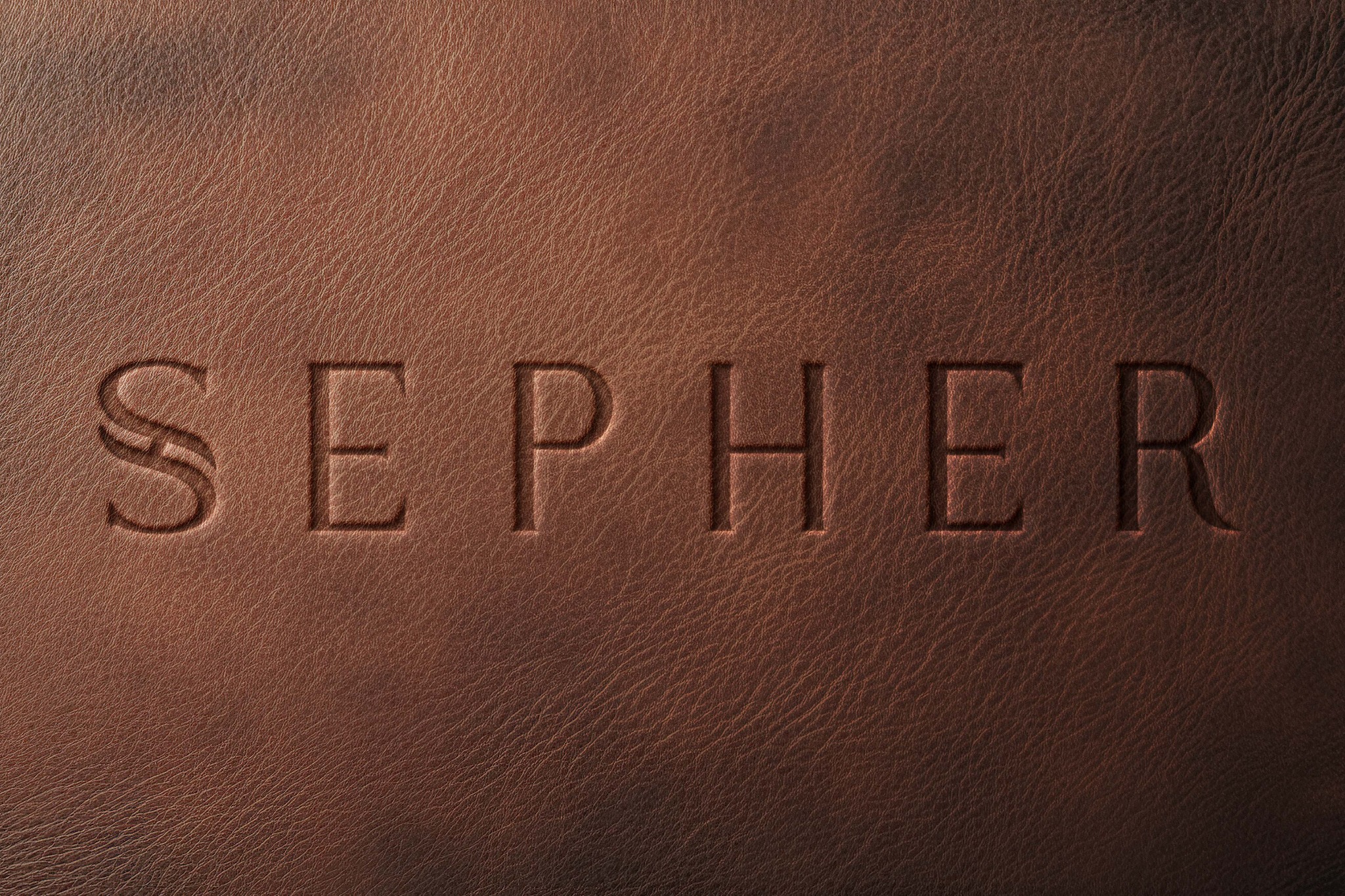 Brązowa skóra z wytłoczonym napisem 'SEPHER', delikatne światło podkreśla fakturę materiału i wgłębienia liter.