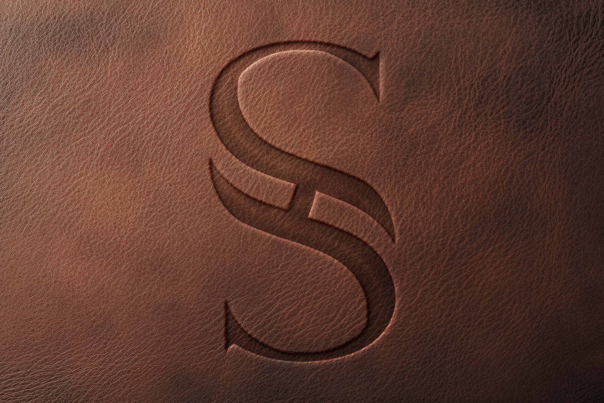 Eleganckie tłoczenie litery 'S' na brązowej skórze, wykonane w Białymstoku. Subtelne cieniowanie podkreśla detale tekstury. Idealne do identyfikacji wizualnej.