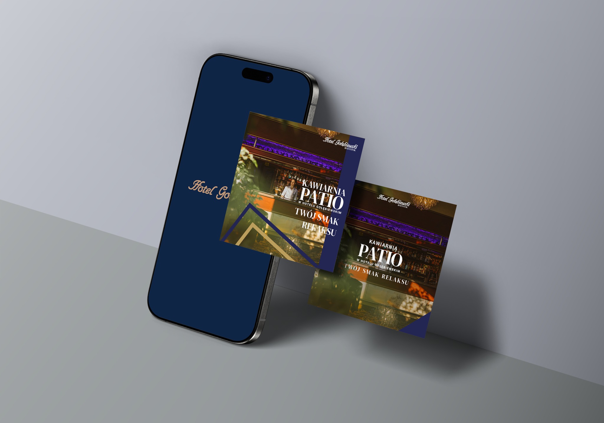 Mockup wizytówki kawiarni Patio Hotelu Gołębiewski na smartfonie z logo hotelu. Grafika reklamowa w odcieniach granatu i złota, prezentacja oferty kawiarni.