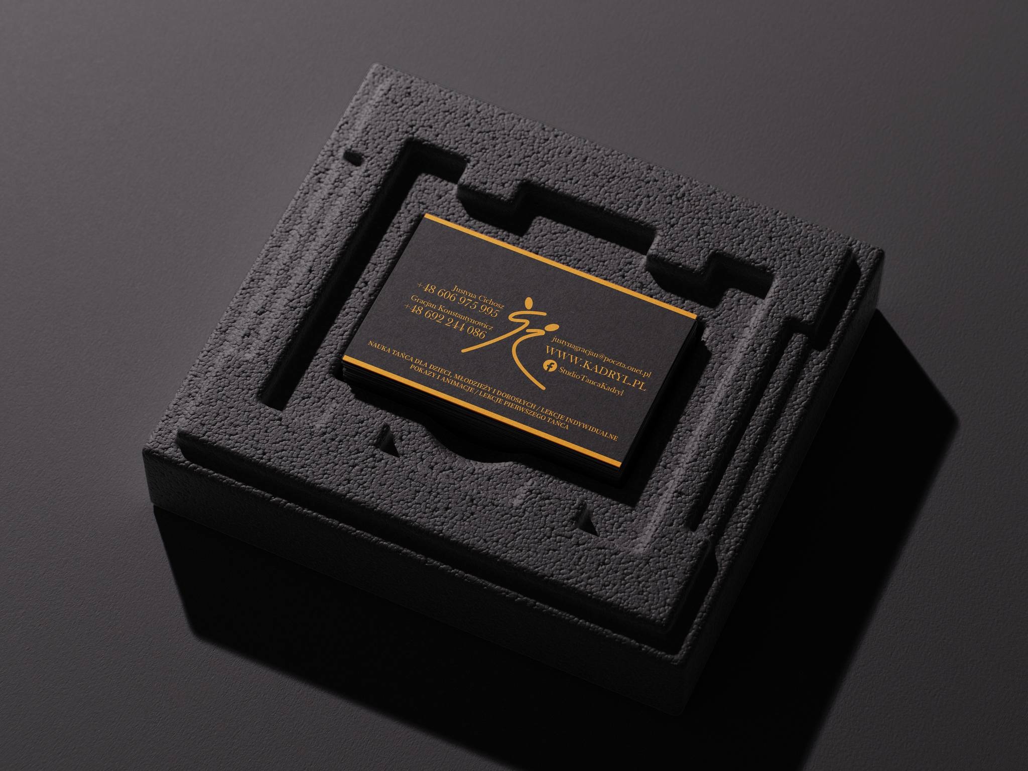 Eleganckie, czarno-złote wizytówki w czarnym, teksturowanym pudełku. Minimalistyczny design, profesjonalny wygląd, oświetlenie podkreśla detale. Studio Tańca Kadryl.