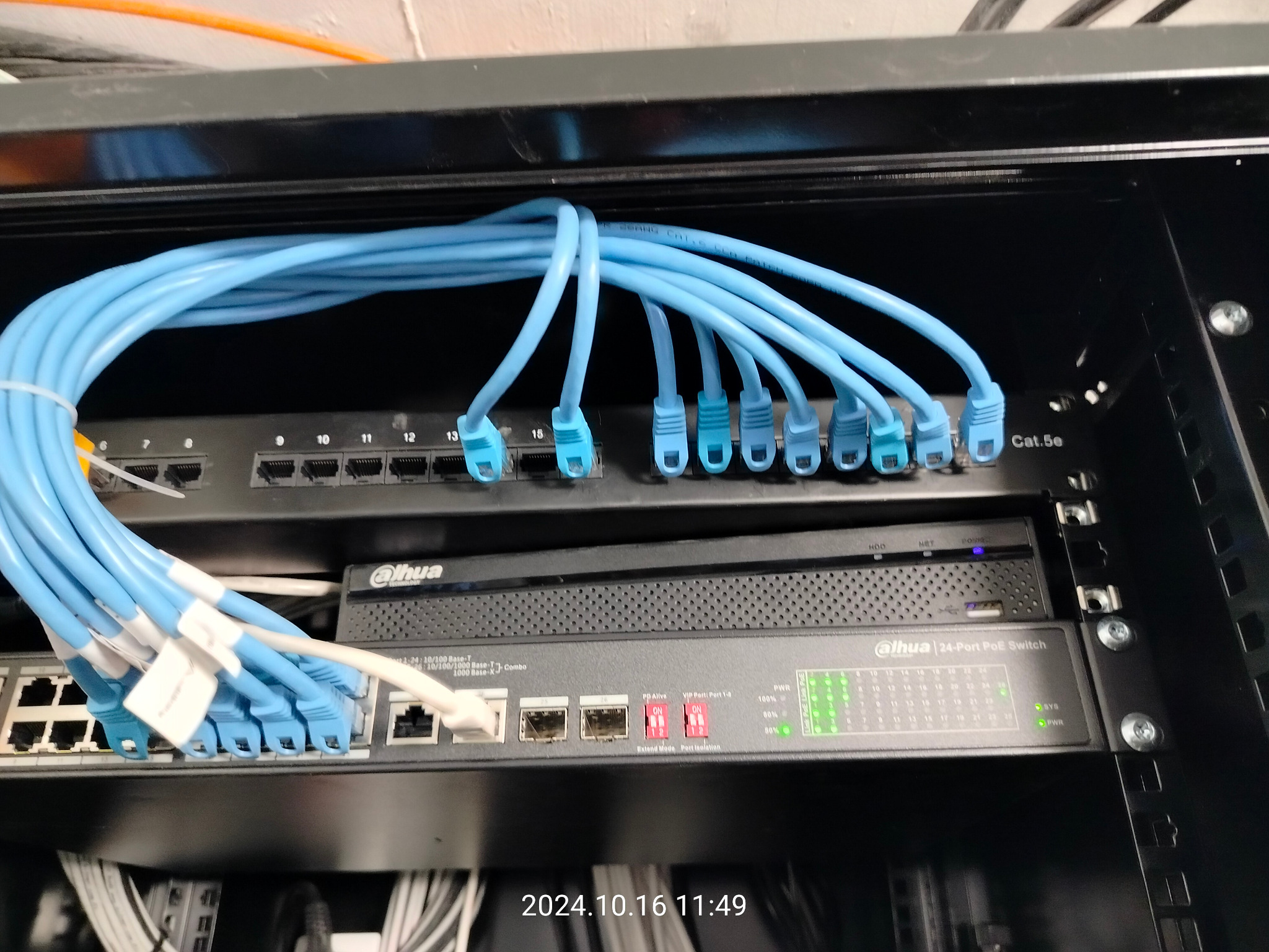 Panel krosowniczy Dahua z podłączonymi niebieskimi kablami sieciowymi Cat.5e w szafie rack. Widoczne porty i diody LED. Instalacja sieciowa w serwerowni.