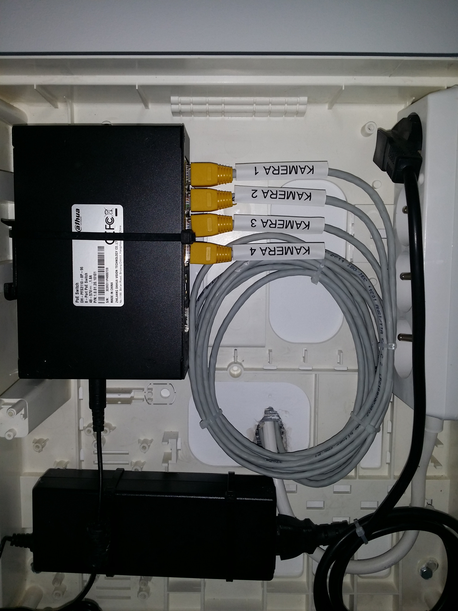 Rozdzielnica z zamontowanym switchem PoE Dahua, zasilaczem i okablowaniem do kamer monitoringu. Kable oznaczone etykietami 'Kamera 1-4'.