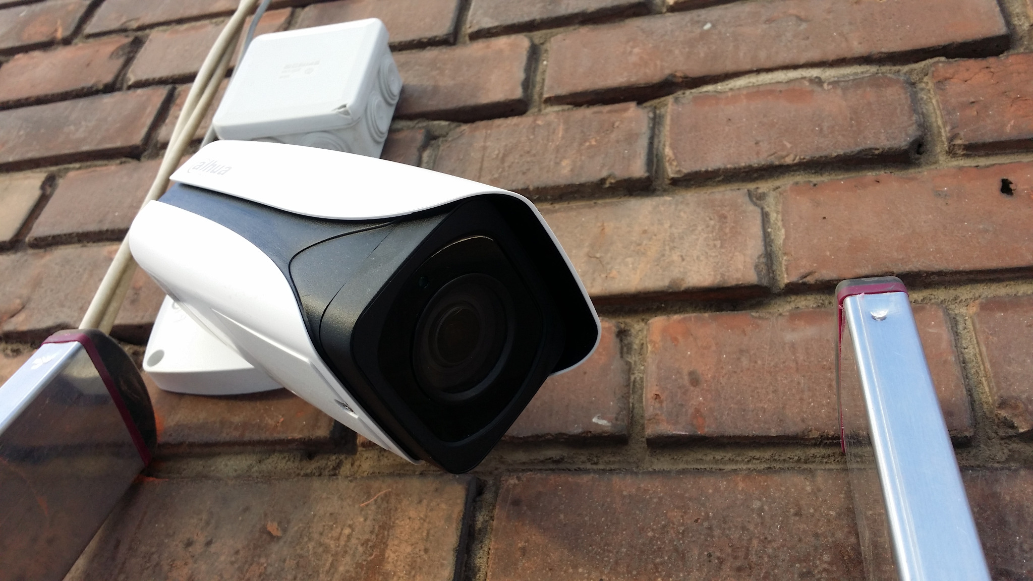 Kamera monitoringu Dahua zamontowana na ceglanej ścianie, widoczna skrzynka przyłączeniowa i fragment drabiny. Ujęcie z dołu, podkreślające solidność instalacji.