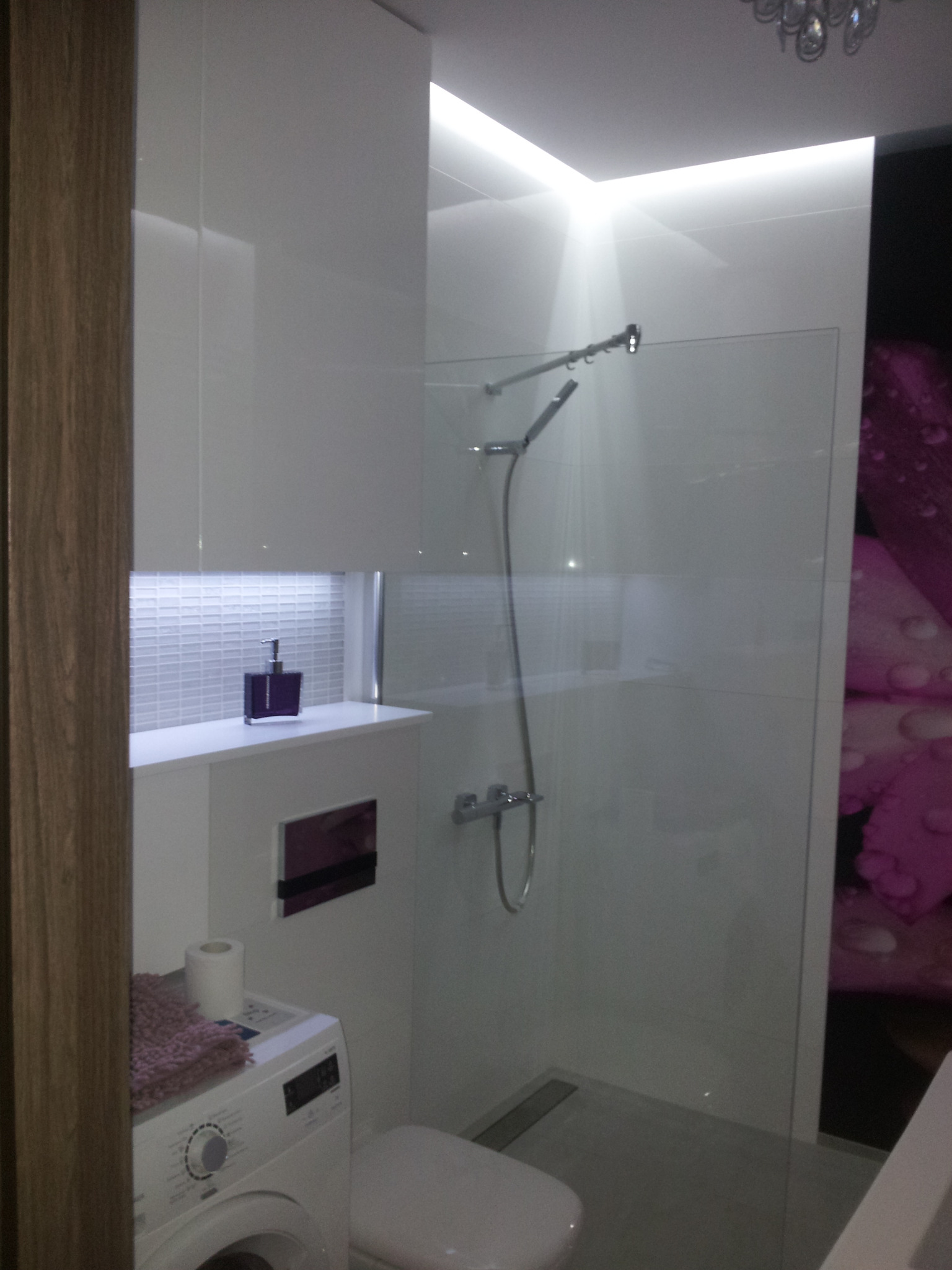 Nowoczesna łazienka z kabiną prysznicową typu walk-in, białą armaturą i akcentami fioletu. Widoczna pralka i mozaika nad blatem. Oświetlenie LED podkreśla minimalistyczny design.