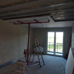 Jan Wróblewski - Wnętrze w trakcie montażu sufitu podwieszanego z płyt gipsowo-kartonowych. Widoczny podnośnik do płyt, drabiny i profile. Częściowo zamontowane płyty.