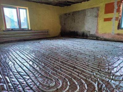 Instalacja ogrzewania podłogowego w pokoju z żółtymi ścianami i oknem. Rury ułożone na folii izolacyjnej, gotowe do zalania wylewką. Widoczne ślady po pracach przygotowawczych.