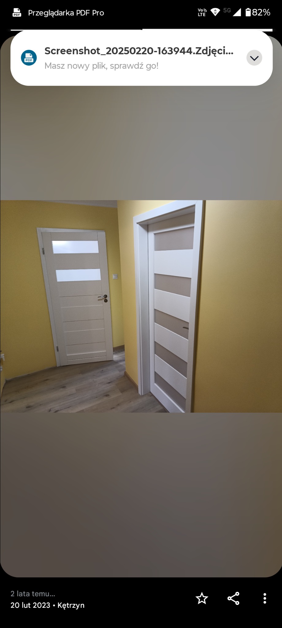 Dwa białe, nowoczesne drzwi z przeszkleniami w żółtym korytarzu. Podłoga wyłożona panelami. Widok na wnętrze po remoncie, z dbałością o detale wykończeniowe.