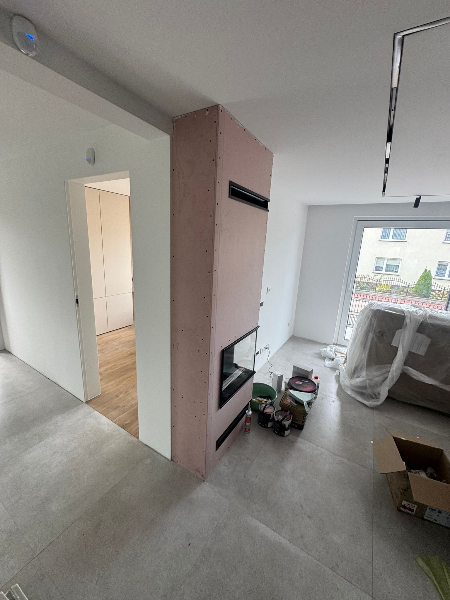 Wnętrze w Zawierciu z kominkiem obudowanym płytą karton-gips, widoczne narzędzia i materiały malarskie. Prace wykończeniowe w trakcie realizacji.