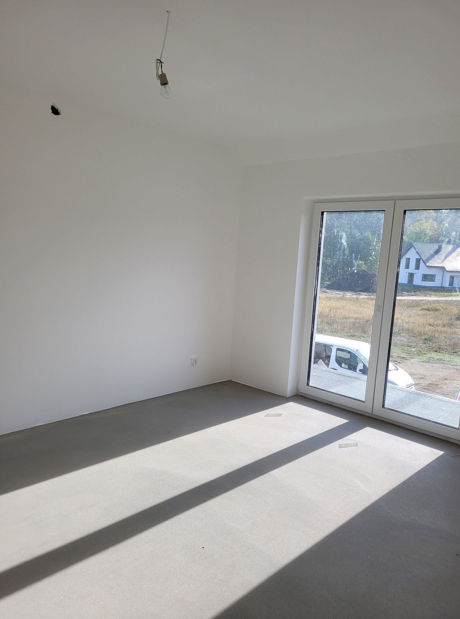 Wnętrze pokoju po wylewce, z widocznymi promieniami słońca wpadającymi przez okno. Na suficie widoczna żarówka na kablu. Ściany pomalowane na biało.