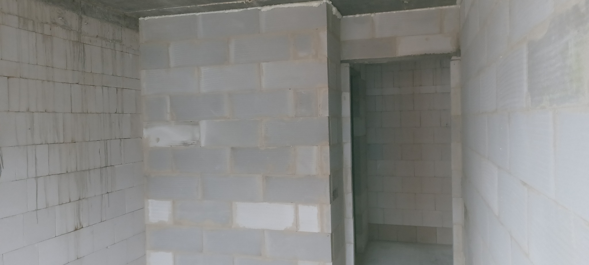 Wnętrze w trakcie budowy: ściany z białych bloczków, widoczny surowy betonowy strop i otwór drzwiowy. Surowy stan wykończenia.