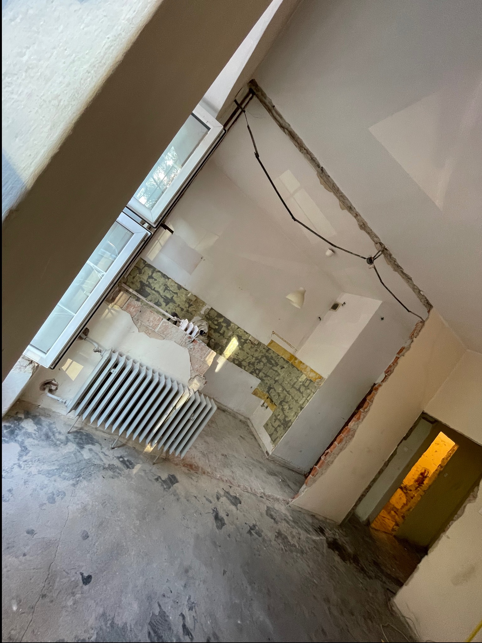 Wnętrze w trakcie rozbiórki: odsłonięte cegły, fragmenty tapet, grzejnik przy oknie. Widoczne ślady po wyburzeniach ścian i przygotowania do dalszych prac remontowych.