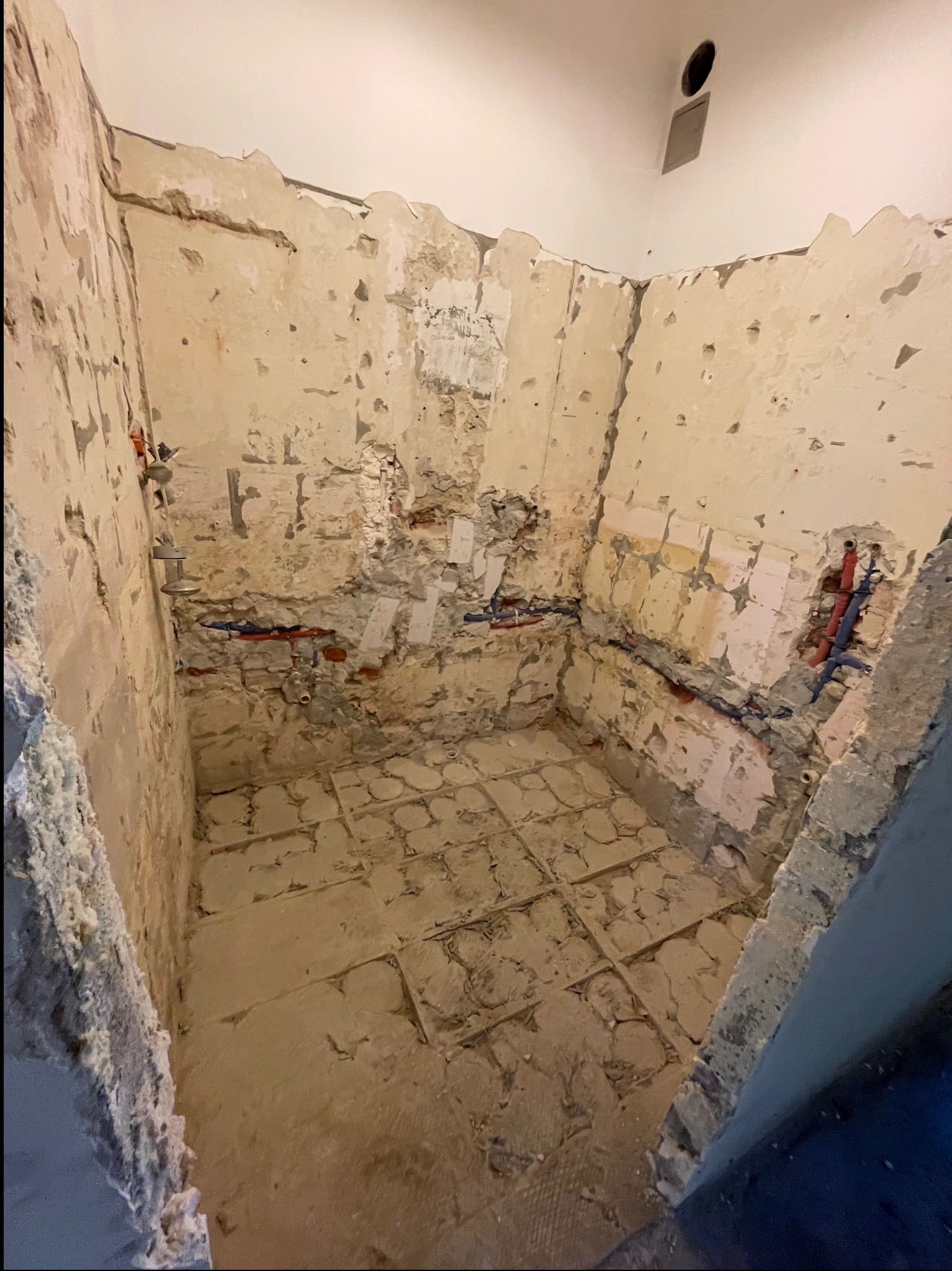 Wnętrze łazienki w trakcie remontu: zerwane płytki, odsłonięte instalacje wodne, ściany z resztkami zaprawy, przygotowane do dalszych prac wykończeniowych. Widok z góry.