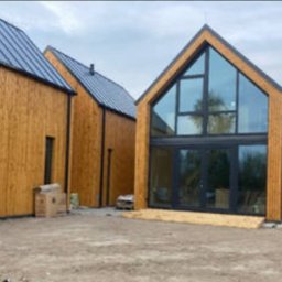 Mar-Motomax Reaktywacja Mariusz Pewniak - Nowoczesny dom z drewnianą elewacją i dużymi przeszkleniami, widok z zewnątrz. Widoczne detale wykończenia i otoczenie budynku.