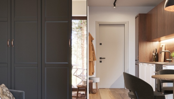 Nowoczesne wnętrze: szara zabudowa szafy z miedzianymi uchwytami, drzwi wejściowe z minimalistyczną klamką i fragment kuchni z drewnianymi szafkami i okrągłym stołem.