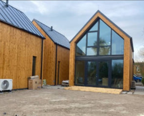 Nowoczesny dom z drewnianą elewacją i dużymi przeszkleniami, widok z zewnątrz. Widoczne detale wykończenia i otoczenie budynku.