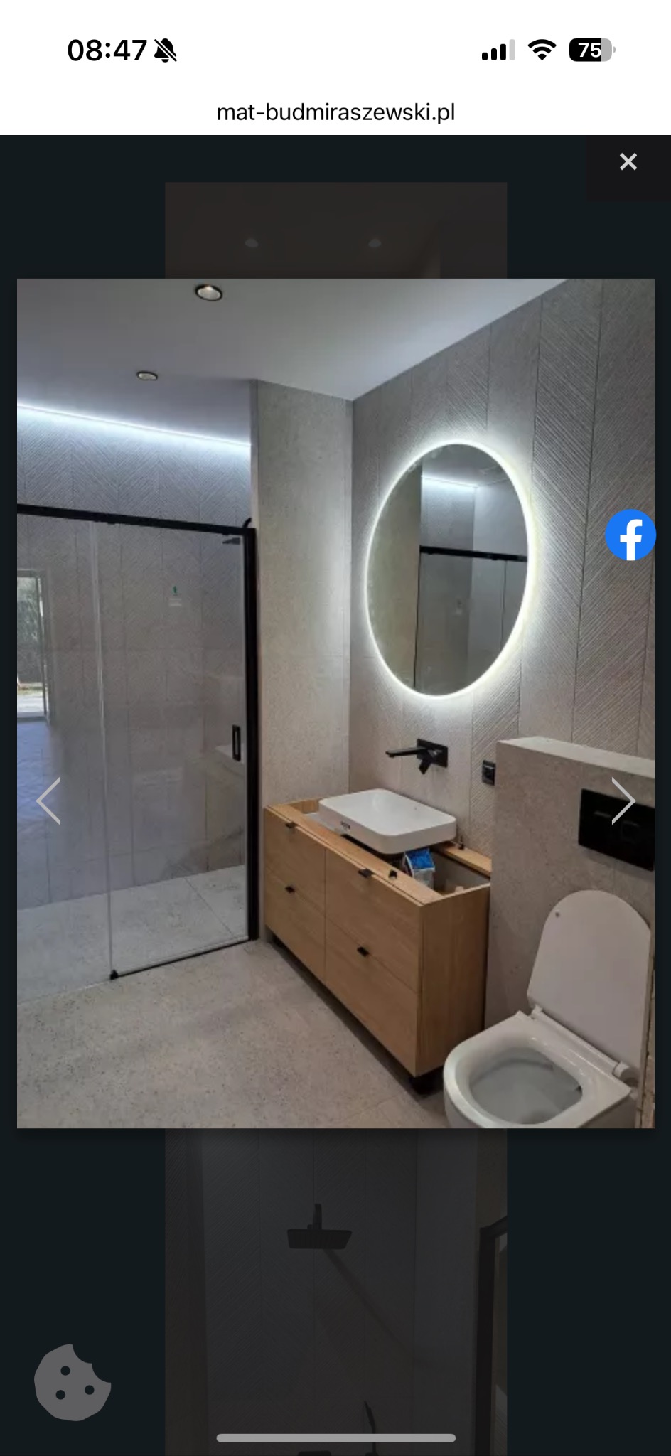 Nowoczesna łazienka z kabiną prysznicową typu walk-in, okrągłym lustrem z podświetleniem LED, drewnianą szafką pod umywalką i wiszącą toaletą.