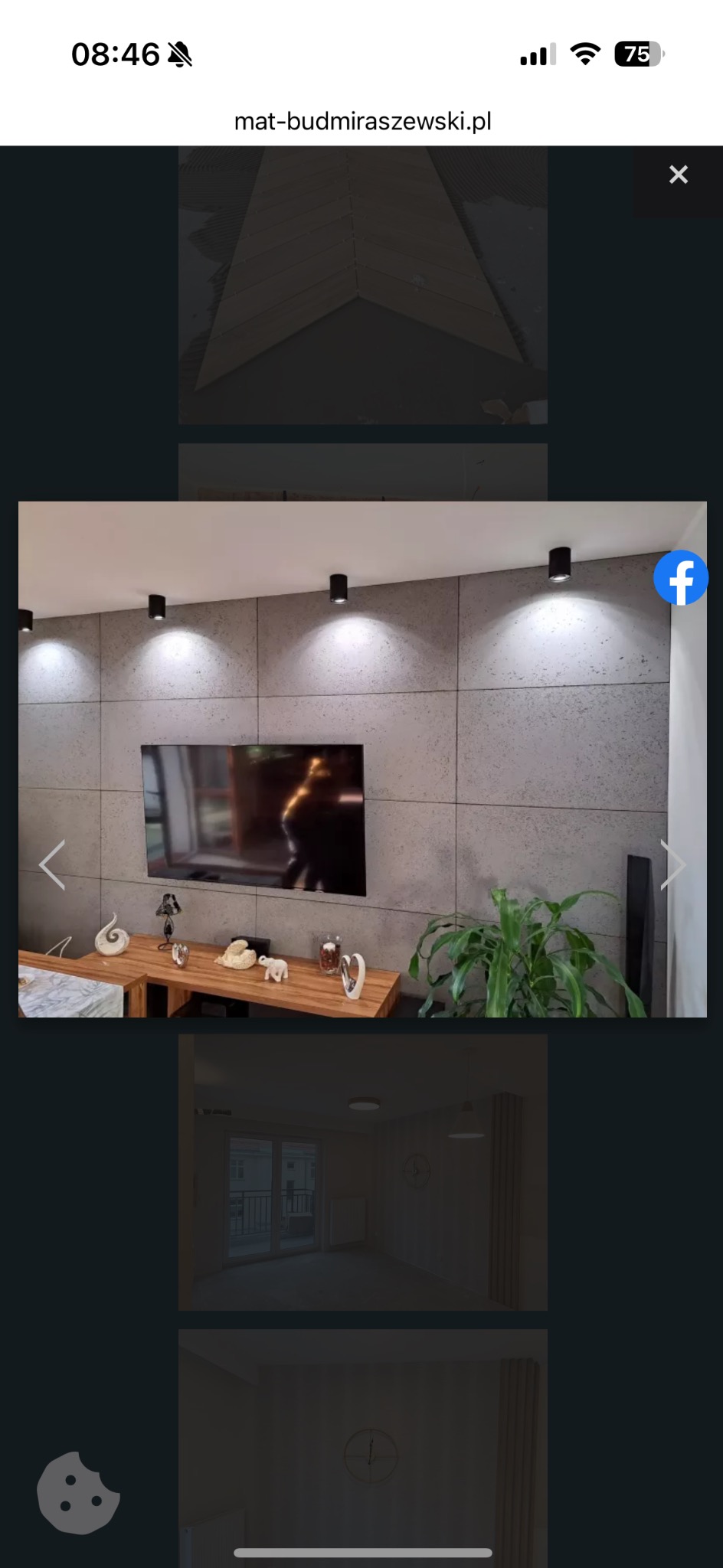 Nowoczesny salon z szarą ścianą imitującą beton, oświetleniem punktowym i drewnianym stolikiem z dekoracjami. Widoczny telewizor i roślina doniczkowa.