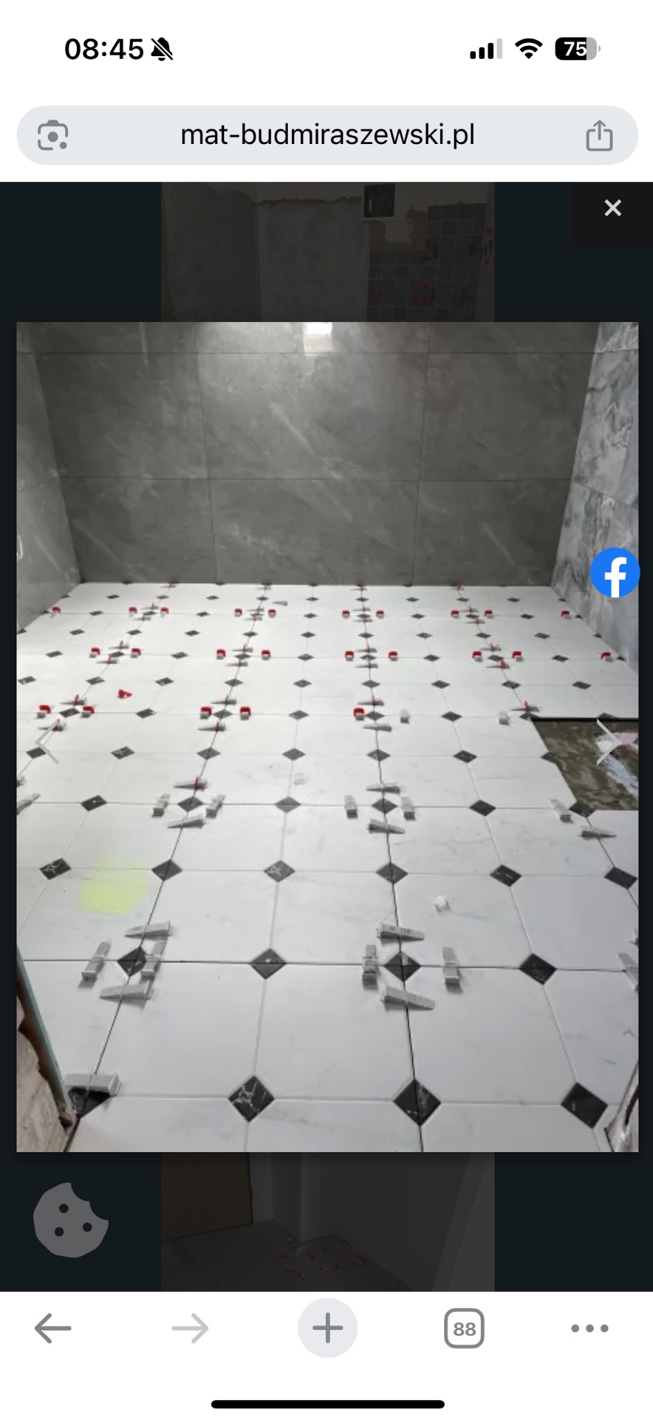 Układanie białych płytek podłogowych z czarnymi akcentami w łazience. Widoczne krzyżyki dystansowe i poziomice. Szare płytki na ścianach.