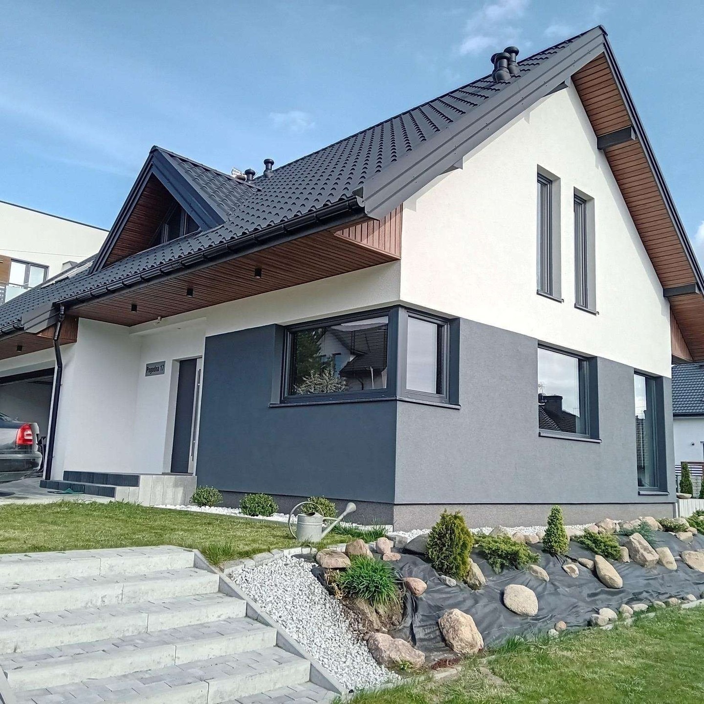 Nowoczesny dom jednorodzinny z grafitowym dachem i elewacją w odcieniach szarości, z minimalistycznym ogrodem i betonowymi schodami wejściowymi.