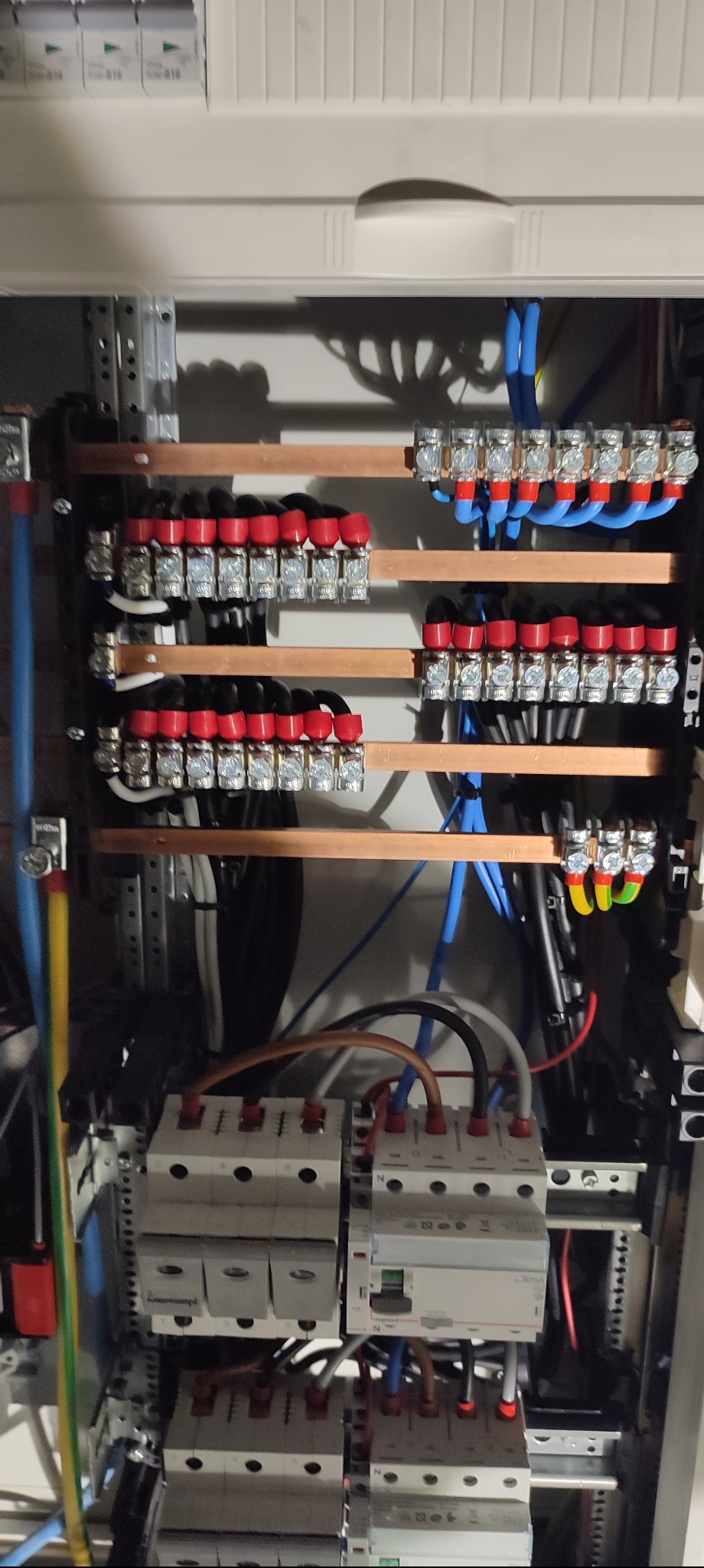 Rozdzielnica elektryczna z widocznymi bezpiecznikami, przewodami i listwami zaciskowymi. Instalacja wykonana schludnie, z użyciem oznaczników na przewodach.