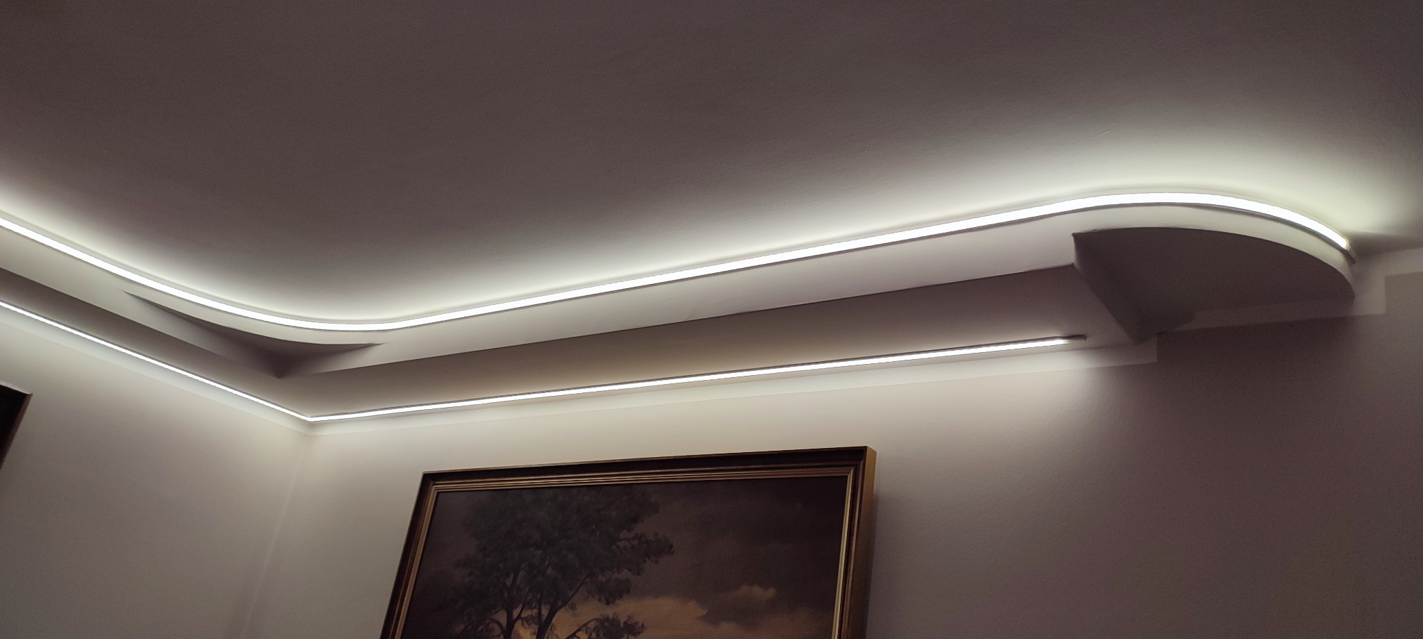 Nowoczesne oświetlenie LED w suficie podwieszanym, z delikatnym światłem podkreślającym architekturę wnętrza. Widoczny fragment obrazu w ramie.