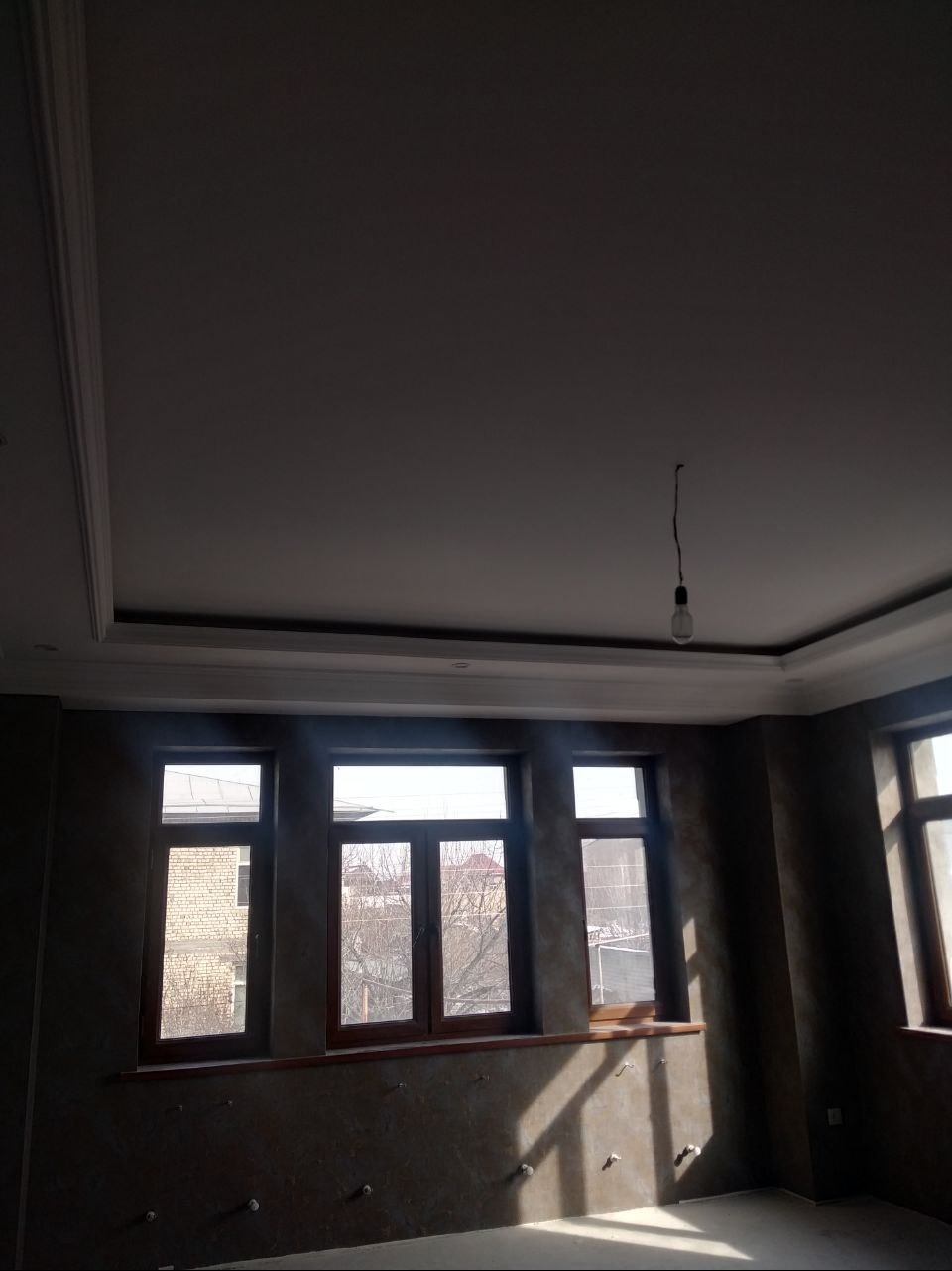 Pokój po gładziowaniu ścian i sufitu z dekoracyjną sztukaterią. Widoczne okna z drewnianą stolarką i wystające kable. Wnętrze w trakcie wykańczania.