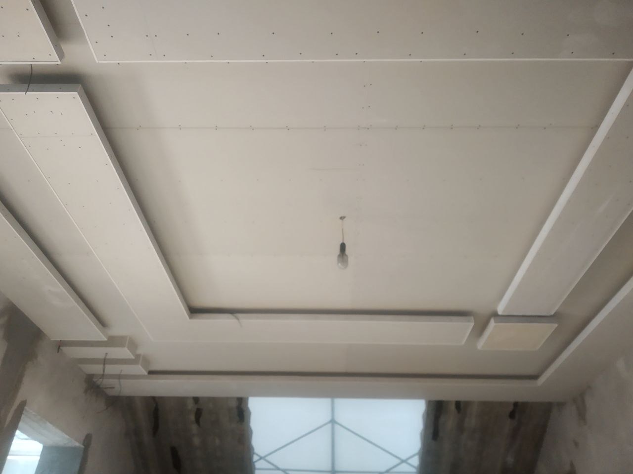 Wykończony sufit z płyt kartonowo-gipsowych z dekoracyjnymi elementami i oświetleniem punktowym w trakcie montażu. Widoczne ślady po szpachlowaniu.