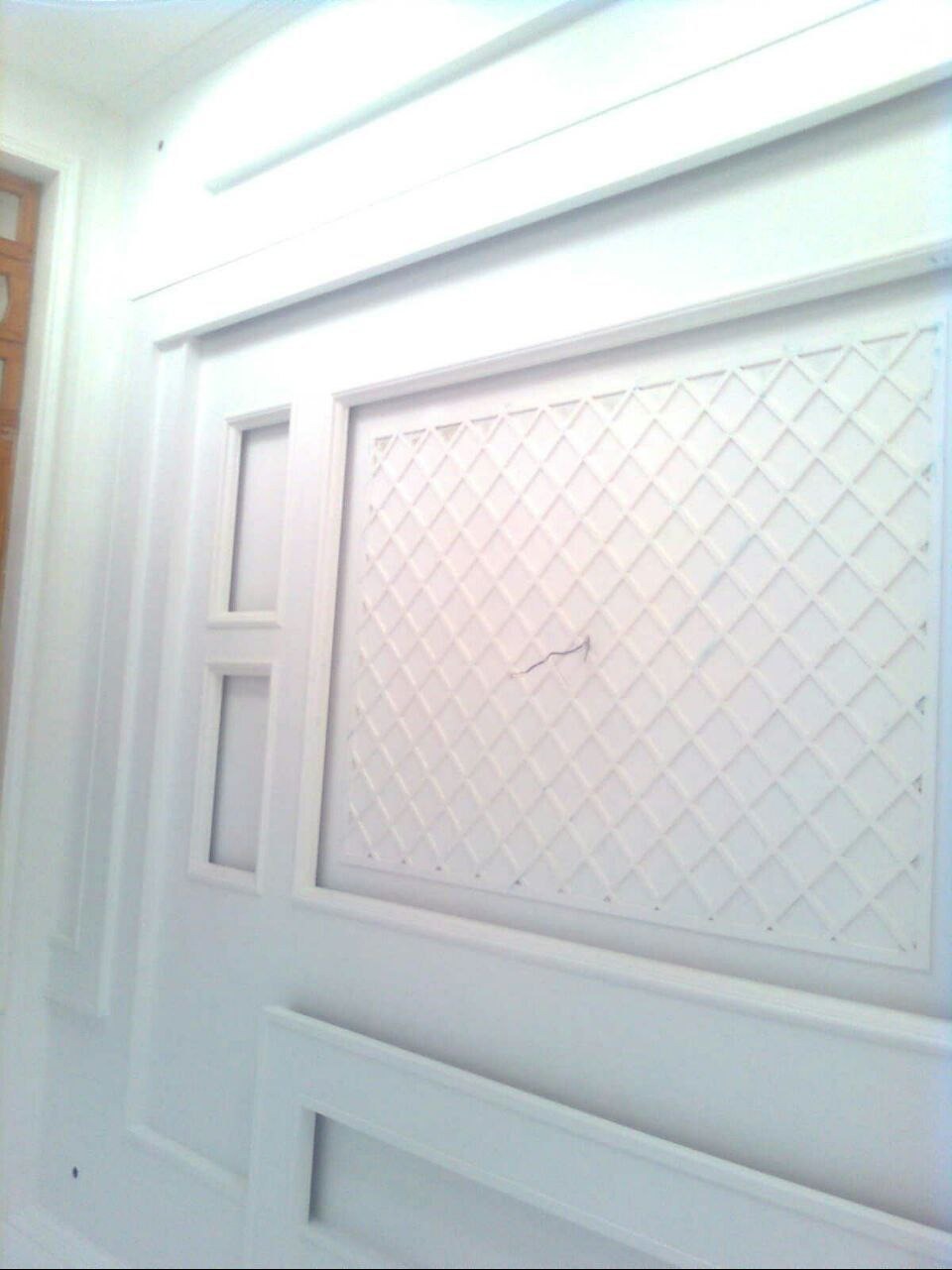 Biała ściana z dekoracyjnym panelem w romby i prostokątnymi wnękami, wykończona listwami. Minimalistyczny design wnętrza, świeżo po remoncie.