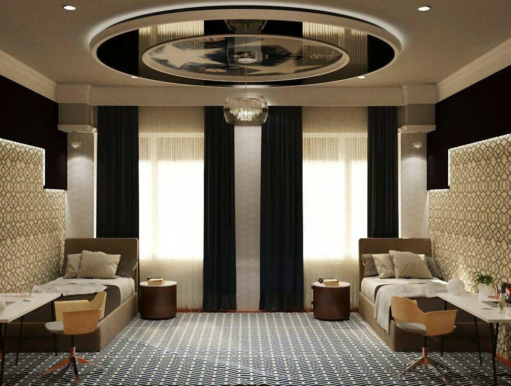 Nowoczesna aranżacja pokoju z dwoma łóżkami, biurkami i dekoracyjnym oświetleniem sufitowym. Geometryczny wzór dywanu i tapety dodaje charakteru wnętrzu.