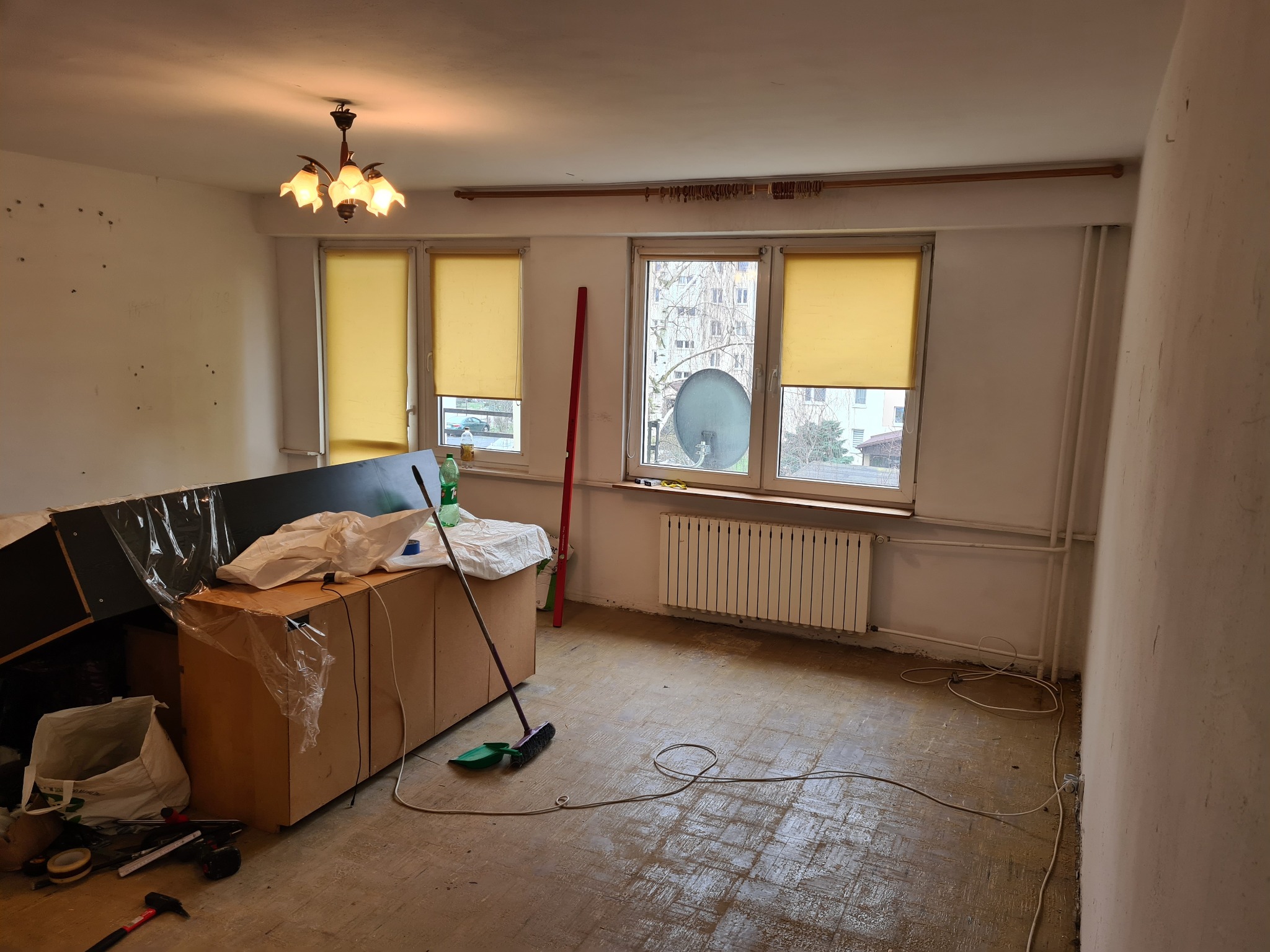 Pokój w trakcie remontu: widoczne narzędzia, meble zabezpieczone folią, ściany przygotowane do malowania, podłoga częściowo zakryta. Przygotowanie do prac wykończeniowych.