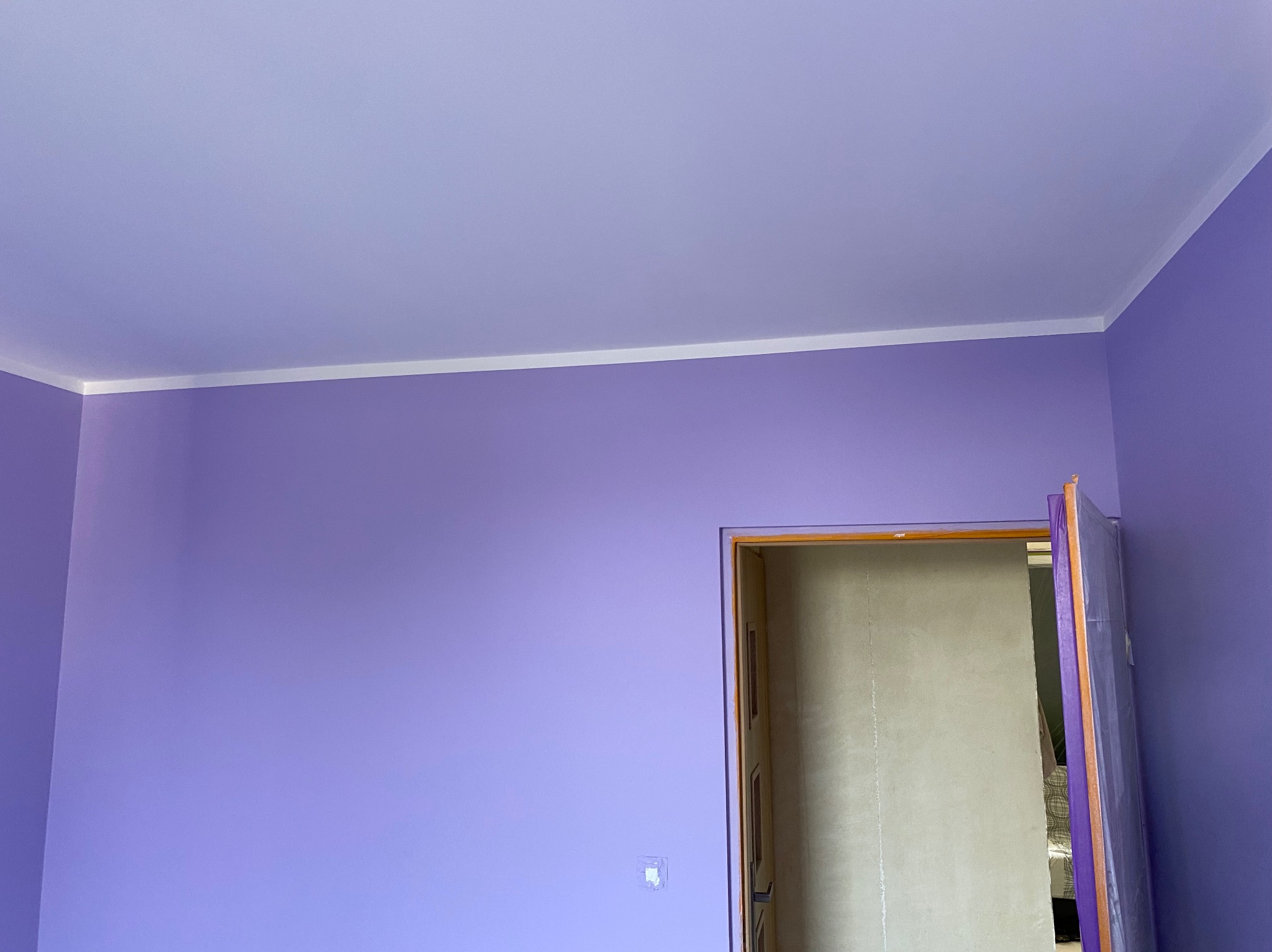 Fioletowe ściany i sufit po malowaniu, biała listwa sufitowa, widok na futrynę drzwiową. Świeżo pomalowane wnętrze z widoczną strukturą farby.