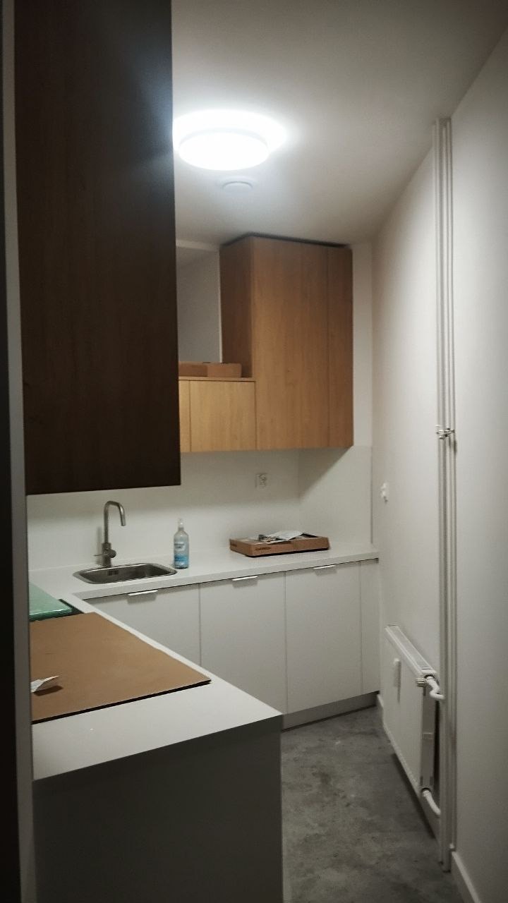 Nowoczesna kuchnia po remoncie: białe szafki, drewniane akcenty, minimalistyczny design i świeżo pomalowane ściany. Widok na grzejnik i fragment blatu roboczego.