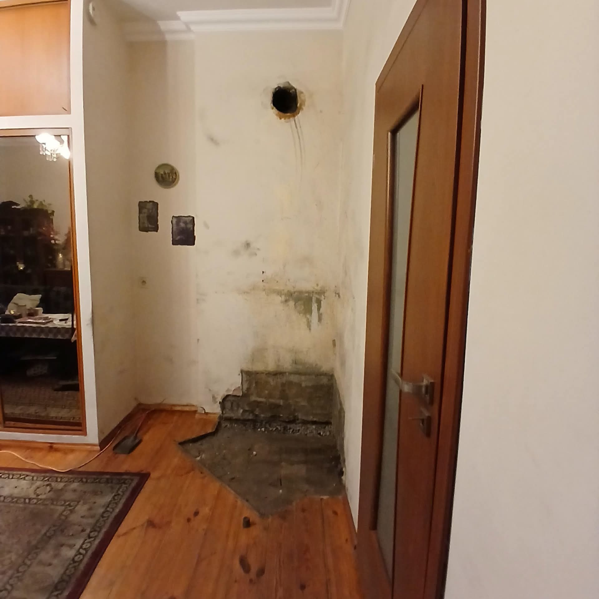 Wnętrze w trakcie demontażu: dziura w ścianie, usunięte fragmenty podłogi, widoczne ślady po instalacjach. Fragment pokoju z drewnianą podłogą i drzwiami.