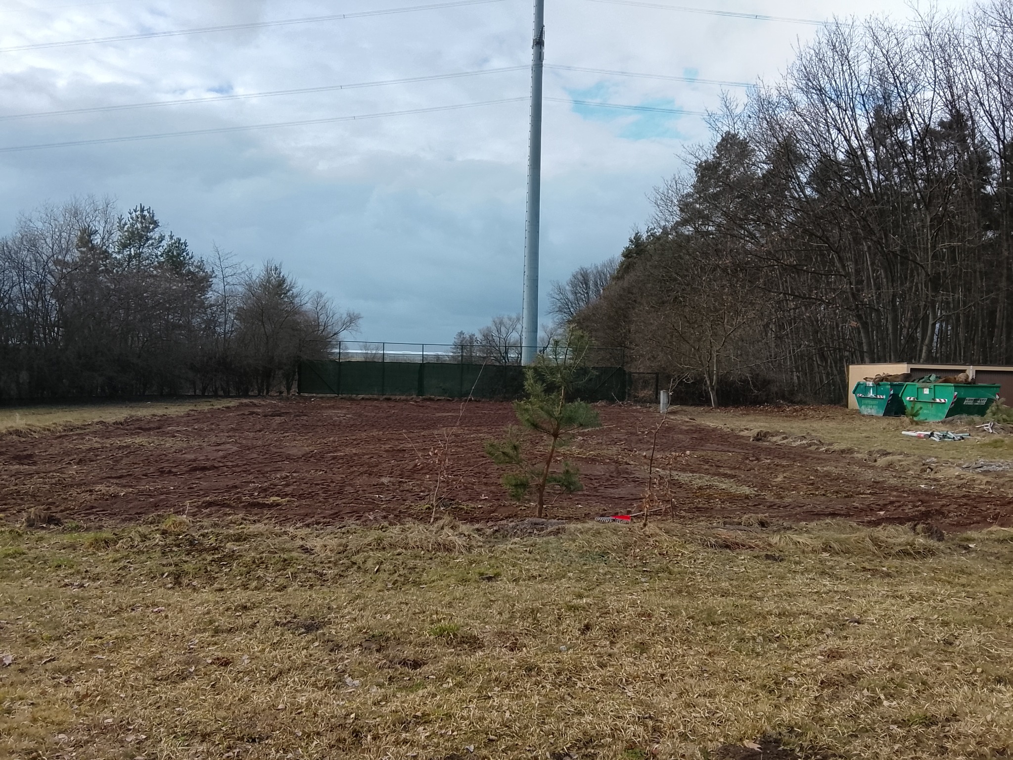 Przygotowany teren pod budowę w Siechnicach. Wyrównana ziemia, widoczne drzewa i kontenery na gruz. W tle słup wysokiego napięcia i zieleń.