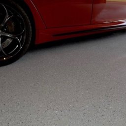 STALLION EPOXY - Szara, błyszcząca posadzka z drobnymi plamkami, obok czerwony samochód Alfa Romeo z widocznym kołem. Gładka powierzchnia, garaż.