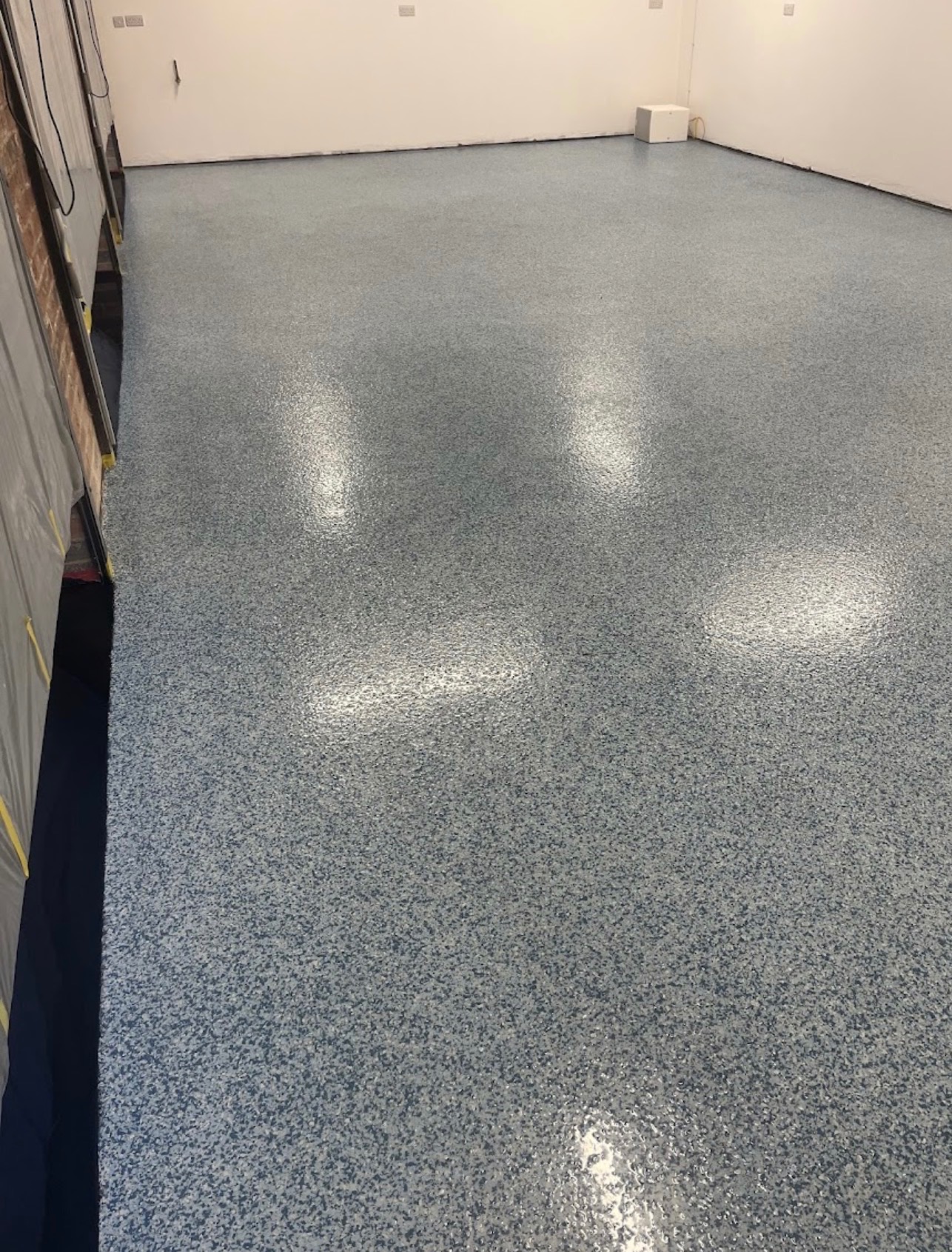 Błękitna posadzka z drobnymi plamkami w pomieszczeniu, wykonana w Łyszkowicach. Widoczne zabezpieczenia ścian folią malarską.