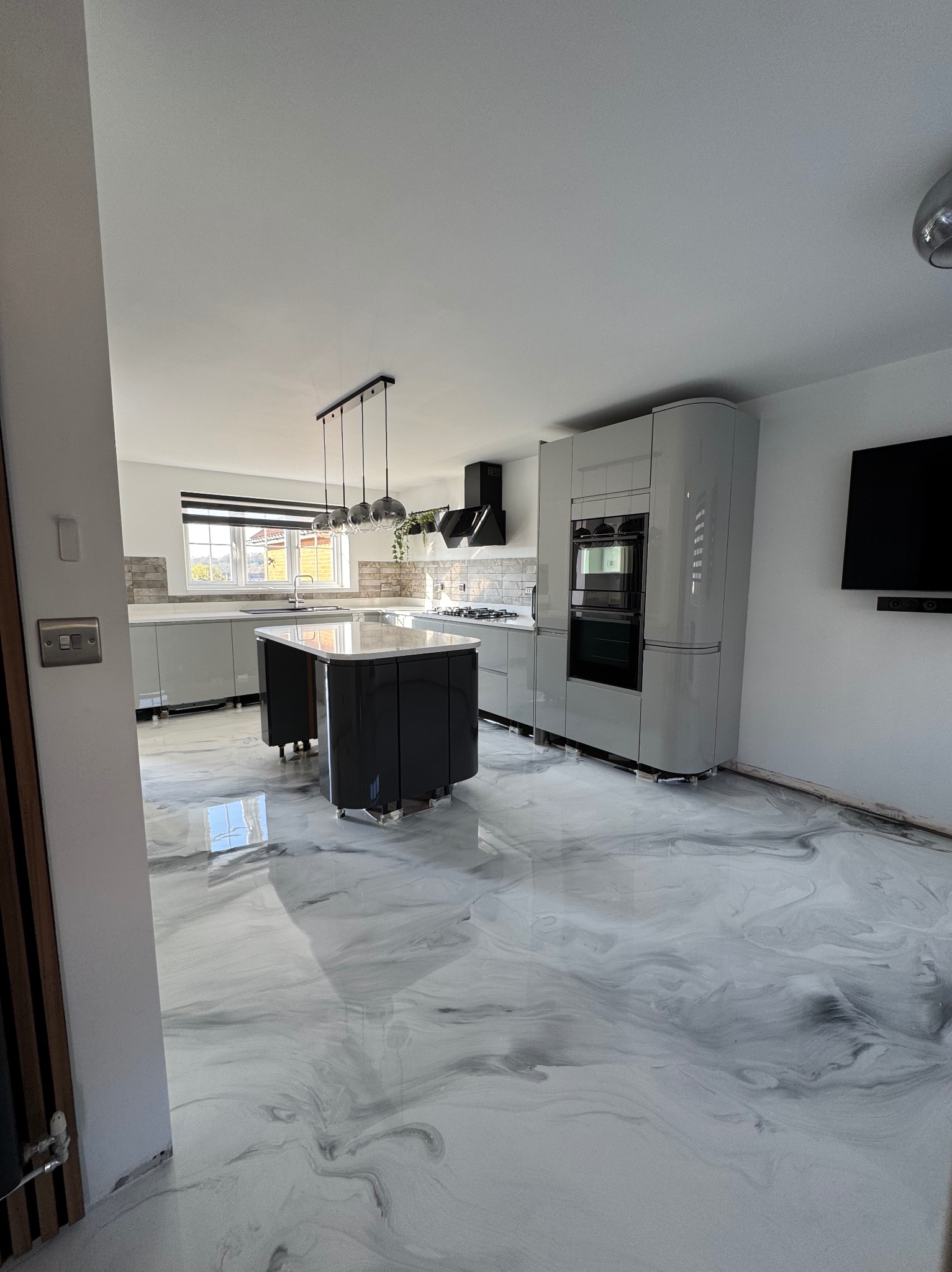 Błyszcząca, szara posadzka z efektem marmuru w nowoczesnej kuchni z wyspą i szarymi szafkami. Widoczne refleksy światła na podłodze, podkreślające jej gładką powierzchnię.