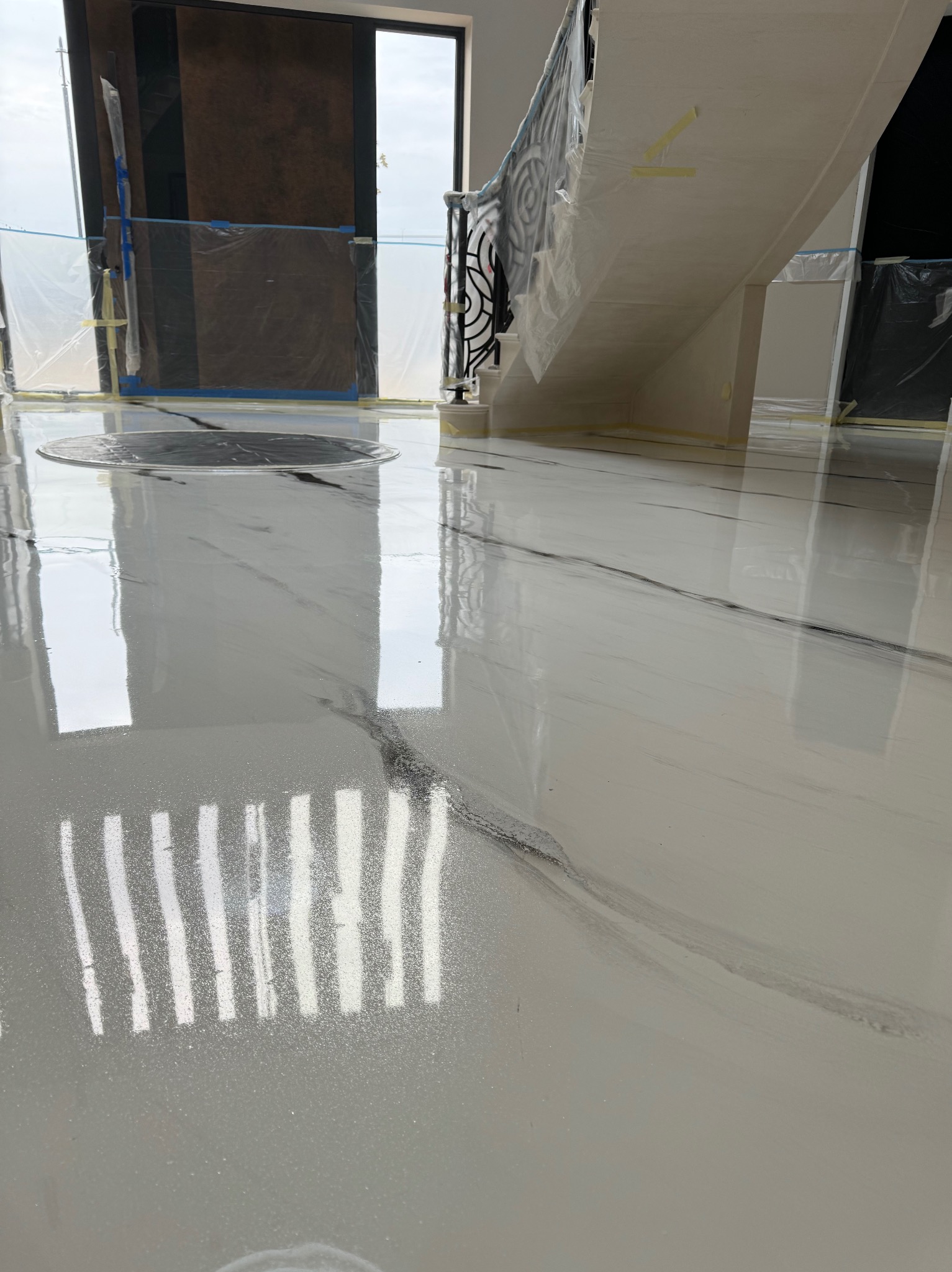 Błyszcząca, biała posadzka z szarymi żyłkami, imitująca marmur, w nowym wnętrzu. Widoczne zabezpieczenia folią malarską przy schodach i drzwiach.