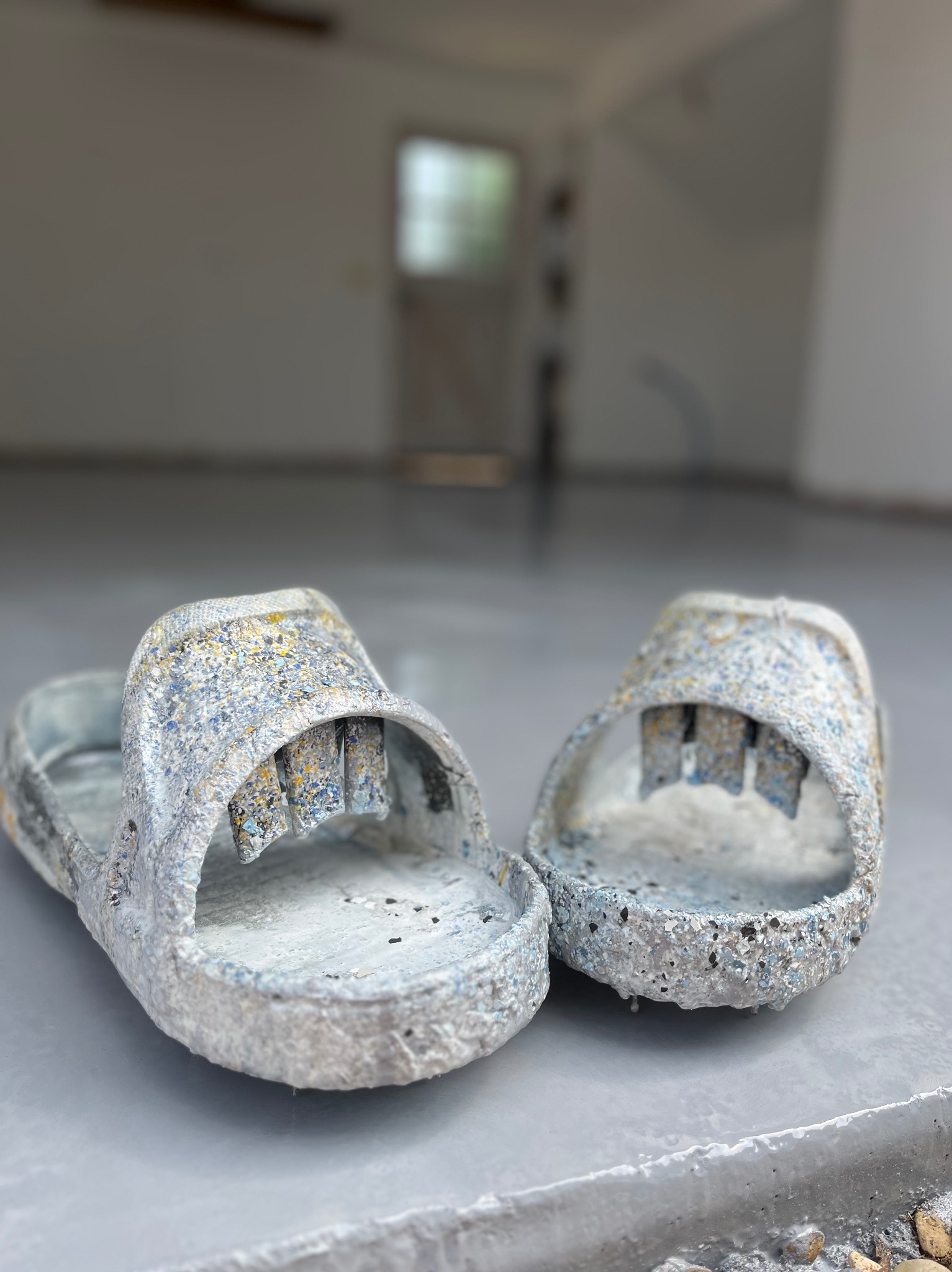 Ślady po pracy: para klapek pokryta resztkami szarej posadzki żywicznej na świeżo wylanej podłodze w garażu. Widoczne drobne kamienie i niedoskonałości.