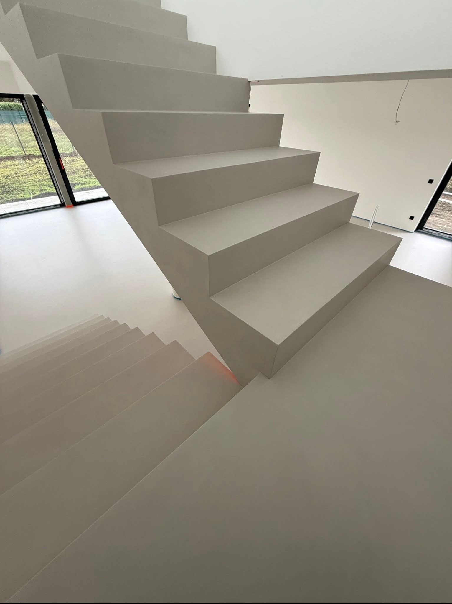 Minimalistyczne, szare schody z mikrocementu w nowoczesnym wnętrzu. Widok z góry, podkreślający gładką powierzchnię i geometryczny kształt stopni.
