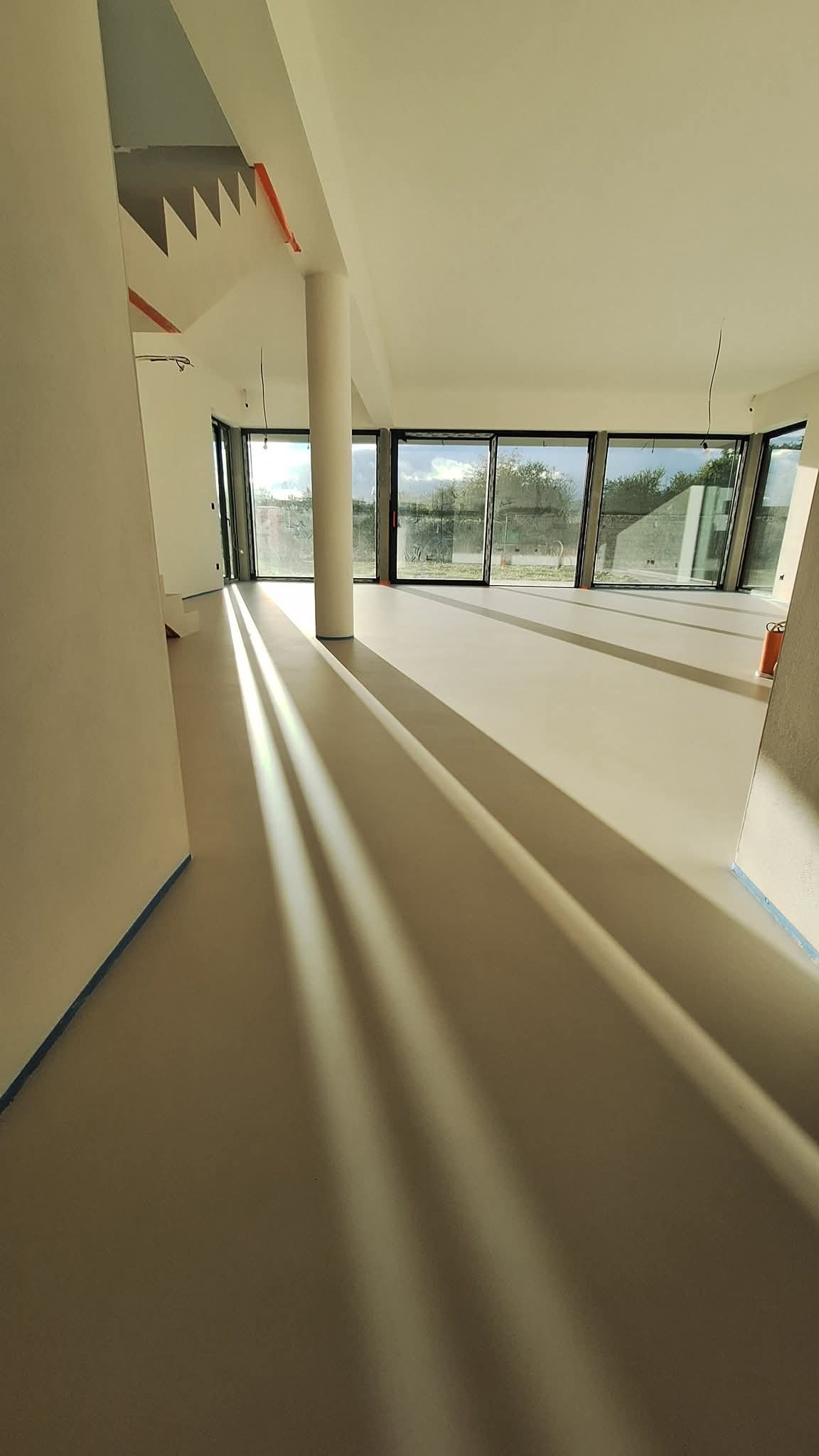 Jasna, gładka posadzka w przestronnym wnętrzu z kolumną i dużymi oknami. Widoczne promienie słoneczne podkreślają jednolitą powierzchnię podłogi.