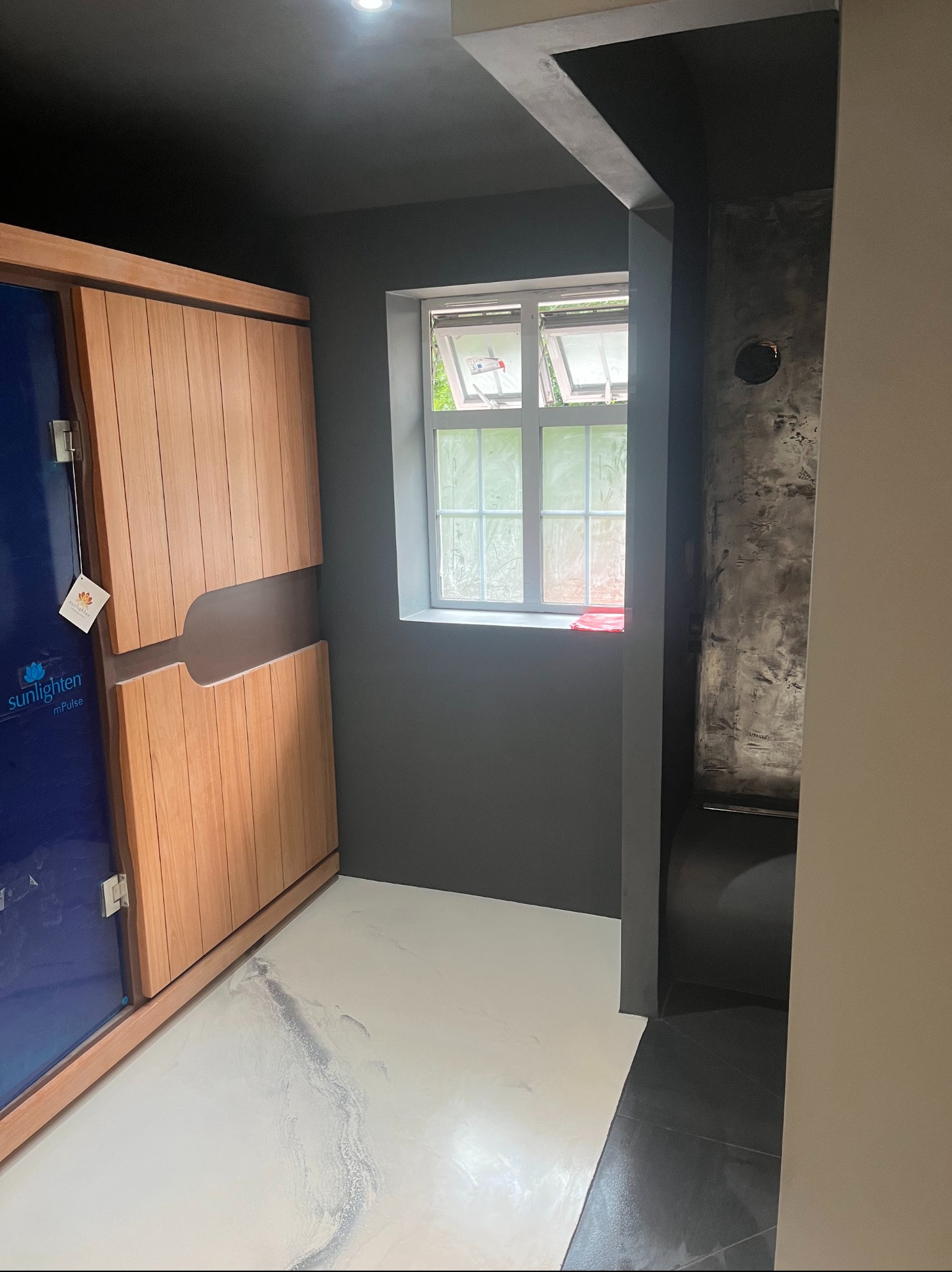 Biała posadzka z efektem marmuru w łazience w Łyszkowicach. Widoczna kabina sauny z drewnianymi drzwiami i okno. Ściany w odcieniach szarości. Nowoczesny design.