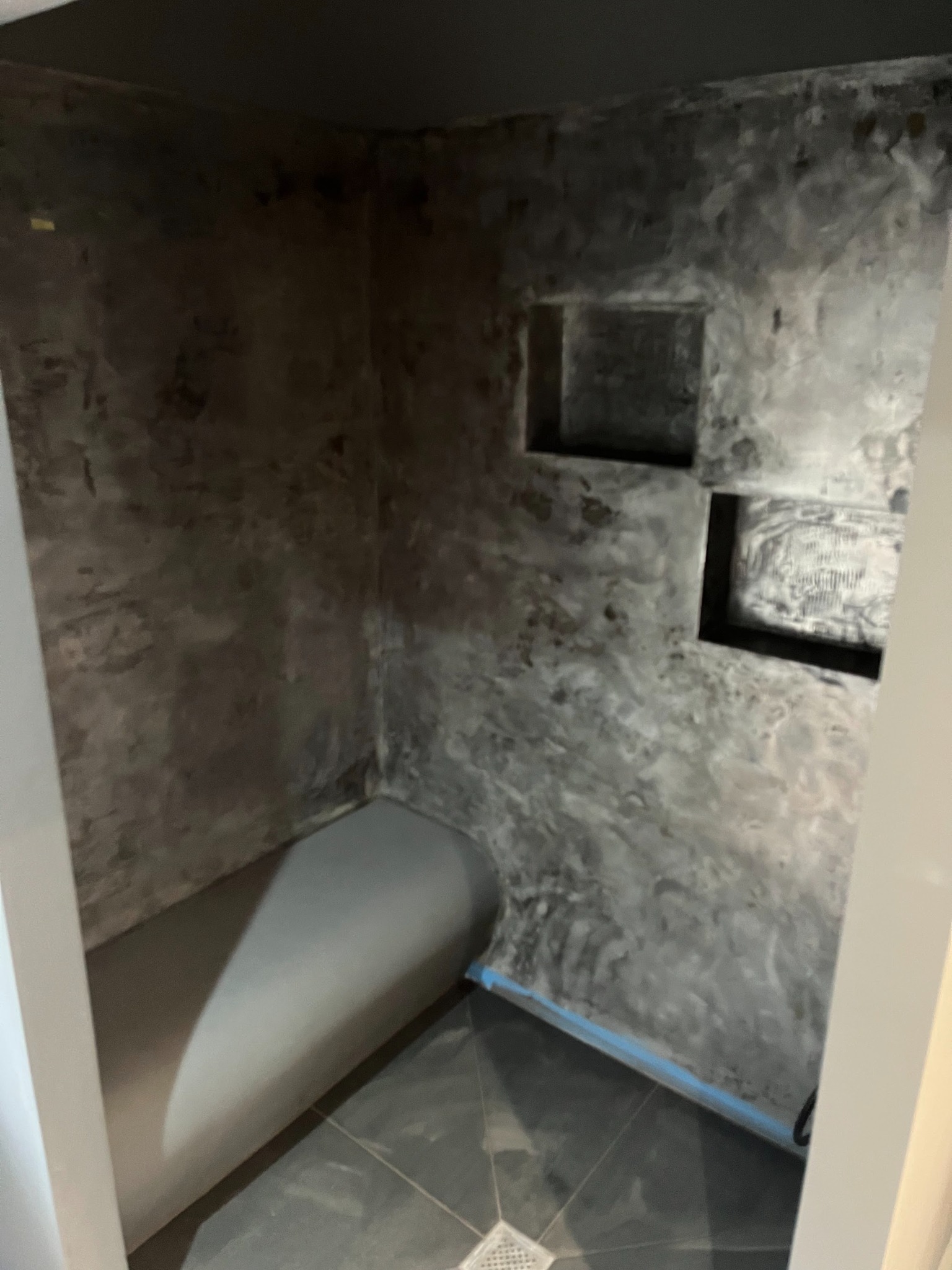 Szara łazienka z mikrocementu z wnękami w ścianie i odpływem liniowym w podłodze. Minimalistyczny design, surowy styl wykończenia.