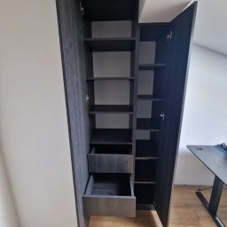 Tomasz Piechota - Szafa wnękowa z szufladami i półkami, wykonana na wymiar do pokoju na poddaszu we Wrocławiu. Ciemne drewno, otwarte drzwi ukazują wnętrze.