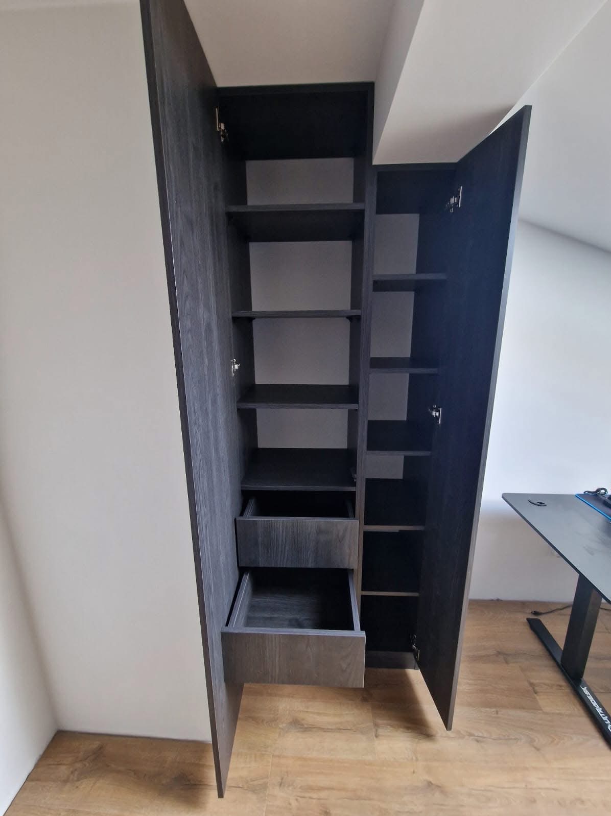 Szafa wnękowa z szufladami i półkami, wykonana na wymiar do pokoju na poddaszu we Wrocławiu. Ciemne drewno, otwarte drzwi ukazują wnętrze.