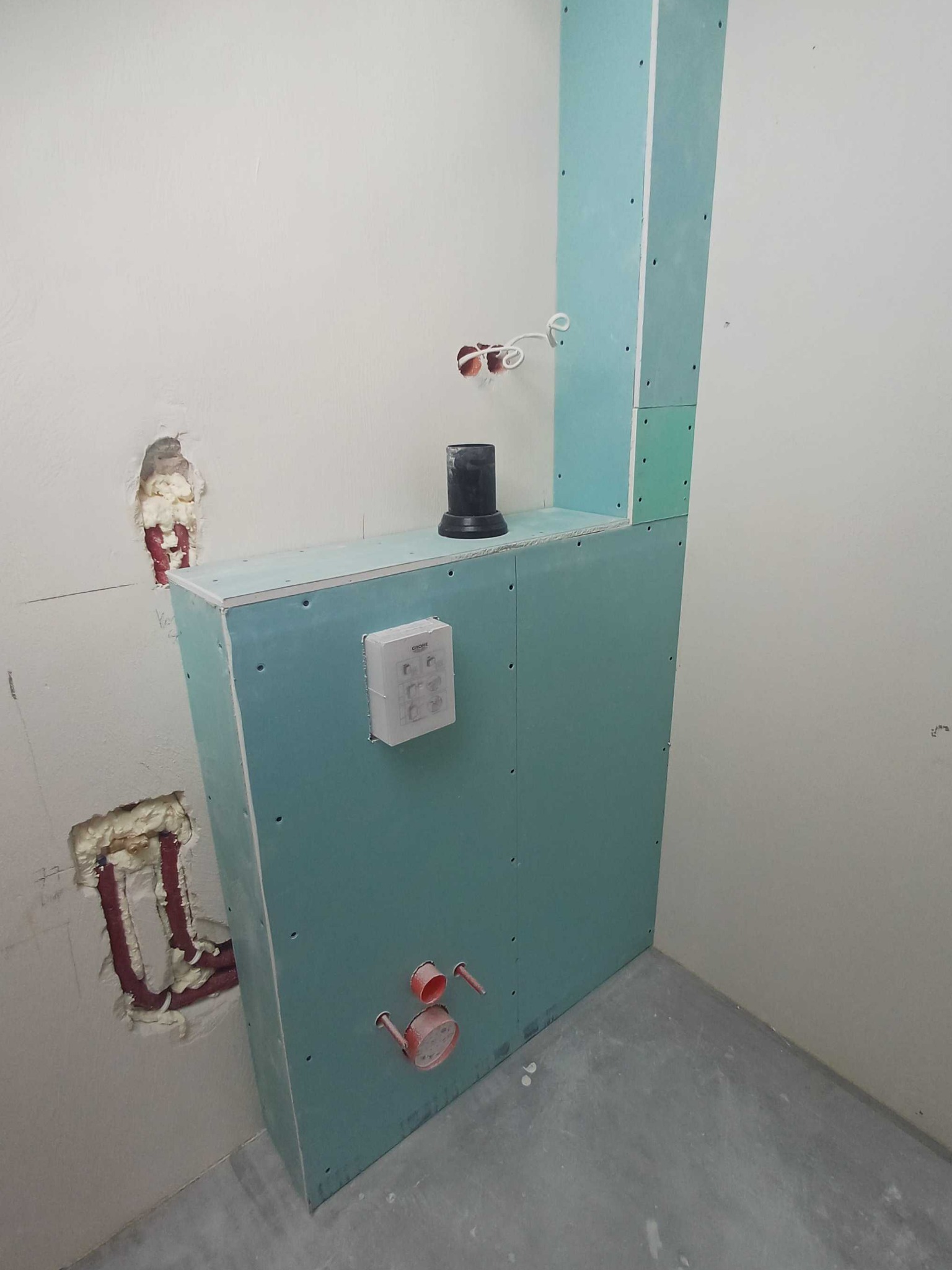 Konstrukcja z płyty karton-gips w łazience, z widocznymi instalacjami wodno-kanalizacyjnymi i elektrycznymi. Etap zabudowy stelaża podtynkowego WC.