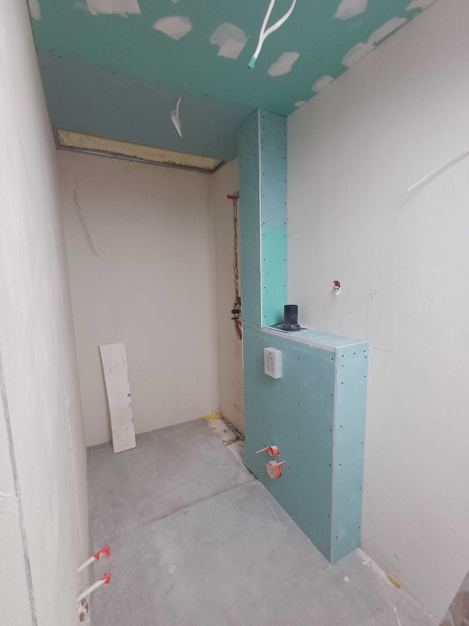Wnętrze w trakcie remontu: zabudowa z płyty karton-gips, sufit z płyt, widoczne instalacje wodne i elektryczne. Szpachlowane ściany, surowy beton na podłodze.