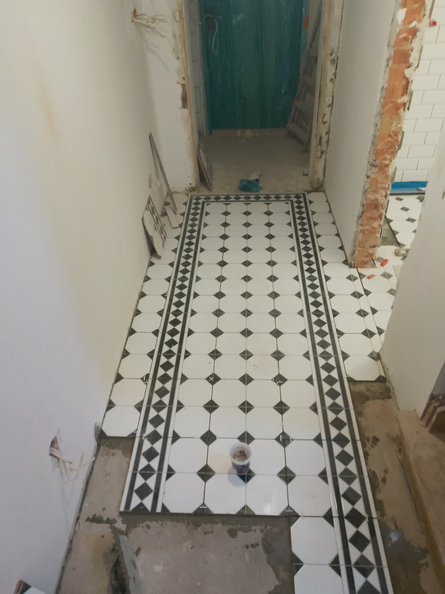 Ułożona podłoga z biało-czarnych płytek w korytarzu podczas remontu. Widoczne krzyżyki dystansowe i niedokończone ściany. Charakterystyczny wzór płytek.