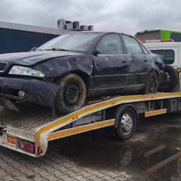 Przemysław Domański - Czarny, uszkodzony samochód Audi A4 na lawecie, z widocznym autobusem Flixbus w tle. Tablica rejestracyjna DSW 99Y4. Widoczne uszkodzenia karoserii.